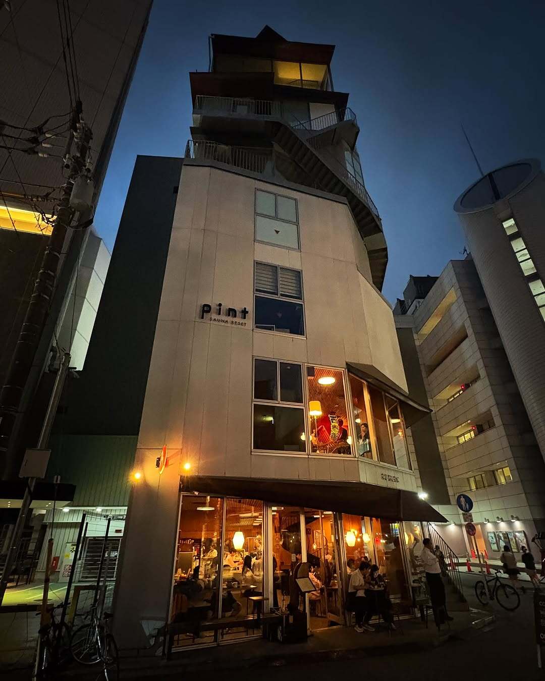 نمای ساختمان ناین آورز آساکوسا در توکیو که طی سال‌های ۲۰۱۸ تا ۲۰۲۵ از هتل کپسولی به برج سونا تغییر کاربری داده و اکنون تنها کافه نروژی FUGLEN در طبقه همکف آن فعال است؛ تصویری مرتبط با معماری و تغییرات کاربری بنا در منطقه آساکوسا.