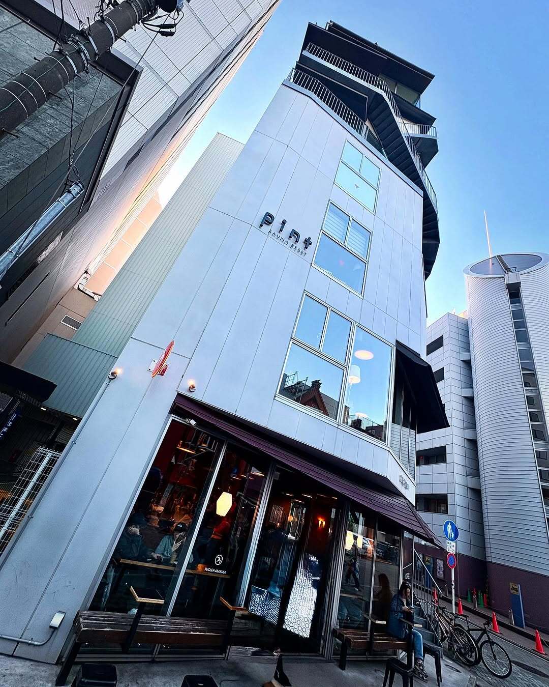 نمای ساختمان ناین آورز آساکوسا در توکیو که طی سال‌های ۲۰۱۸ تا ۲۰۲۵ از هتل کپسولی به برج سونا تغییر کاربری داده و اکنون تنها کافه نروژی FUGLEN در طبقه همکف آن فعال است؛ تصویری مرتبط با معماری و تغییرات کاربری بنا در منطقه آساکوسا.