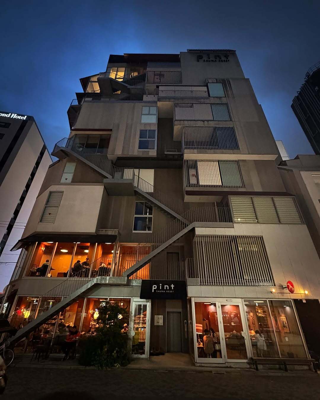 نمای ساختمان ناین آورز آساکوسا در توکیو که طی سال‌های ۲۰۱۸ تا ۲۰۲۵ از هتل کپسولی به برج سونا تغییر کاربری داده و اکنون تنها کافه نروژی FUGLEN در طبقه همکف آن فعال است؛ تصویری مرتبط با معماری و تغییرات کاربری بنا در منطقه آساکوسا.