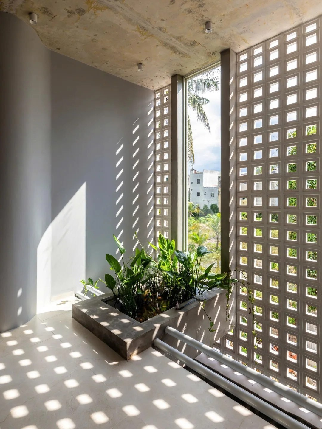 نمای خارجی و داخلی خانه چهار طبقه «شهر غربی» (Casa Cidade do Oeste) در ویتنام با مساحت ۹۰ متر مربع، که طراحی آن شامل نمای ساده، لایه‌های انبوه گیاهی برای حفظ حریم خصوصی، و فضاهای داخلی پلان باز با نورگیر مرکزی برای ایجاد محیطی آرام و روشن است.