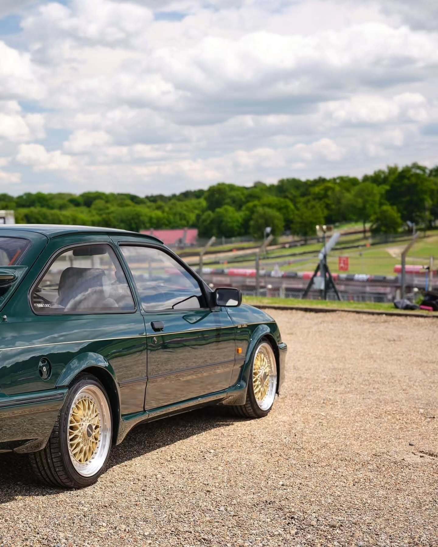 تصویر تمام‌قد و با زاویه باز از خودروی کلاسیک و اسپرت فورد سیرا کاسورث (Ford Sierra Cosworth) با رنگ تیره، که باله عظیم عقب و گلگیرهای برجسته آن در دهه ۱۹۸۰ میلادی آن را به یک نماد سرعت و سلطه بر پیست‌های مسابقه تبدیل کرد.