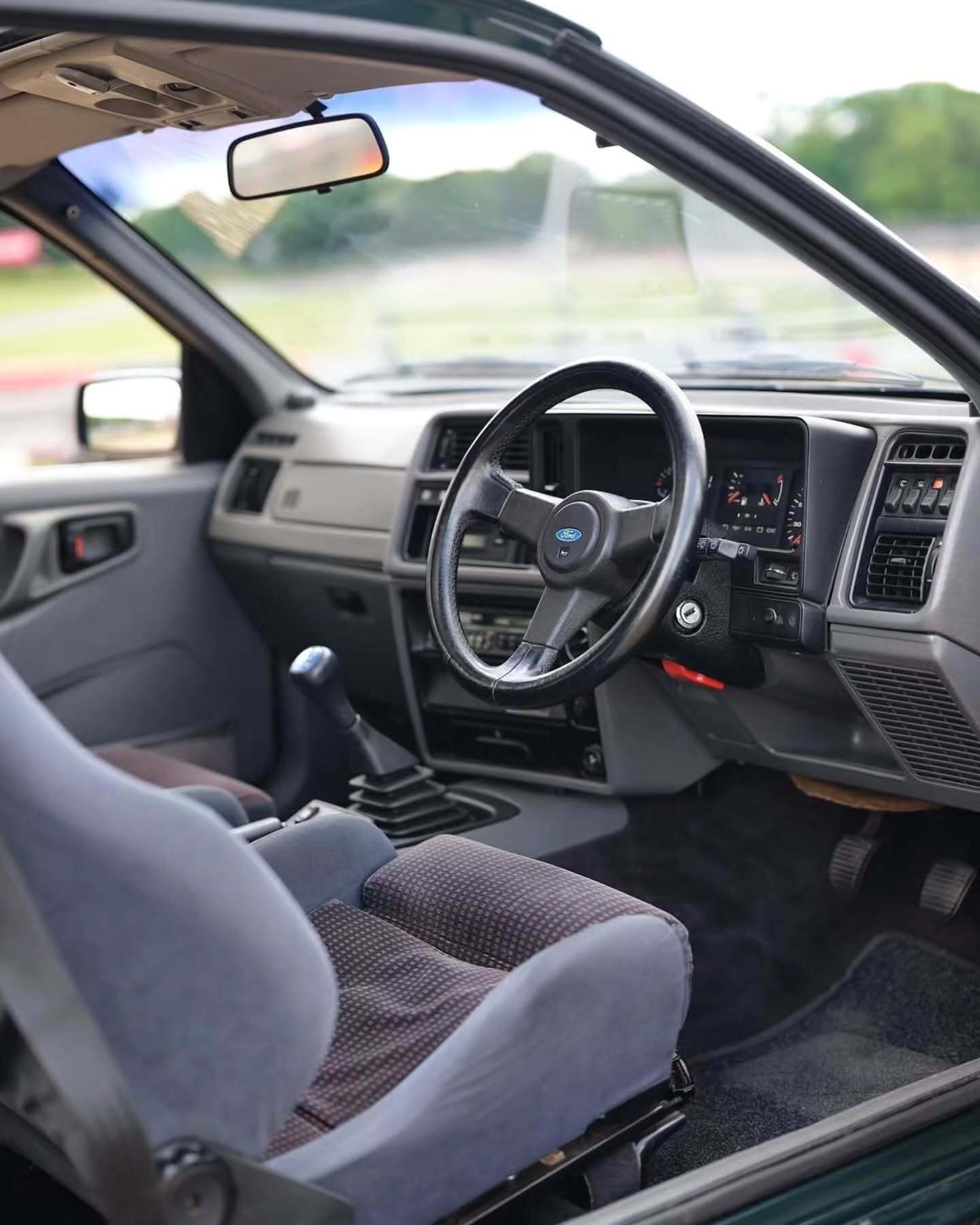 تصویر تمام‌قد و با زاویه باز از خودروی کلاسیک و اسپرت فورد سیرا کاسورث (Ford Sierra Cosworth) با رنگ تیره، که باله عظیم عقب و گلگیرهای برجسته آن در دهه ۱۹۸۰ میلادی آن را به یک نماد سرعت و سلطه بر پیست‌های مسابقه تبدیل کرد.