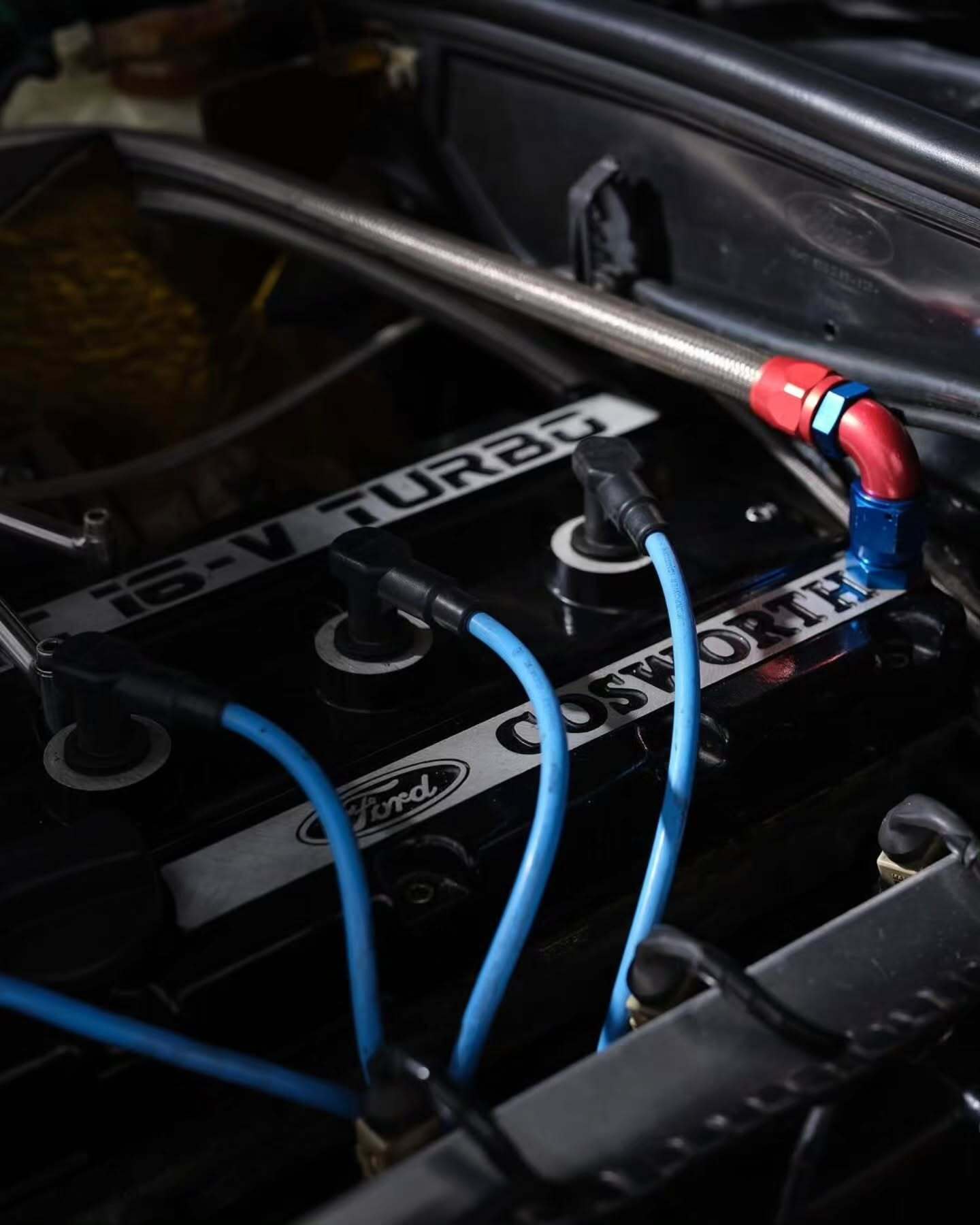 تصویر تمام‌قد و با زاویه باز از خودروی کلاسیک و اسپرت فورد سیرا کاسورث (Ford Sierra Cosworth) با رنگ تیره، که باله عظیم عقب و گلگیرهای برجسته آن در دهه ۱۹۸۰ میلادی آن را به یک نماد سرعت و سلطه بر پیست‌های مسابقه تبدیل کرد.