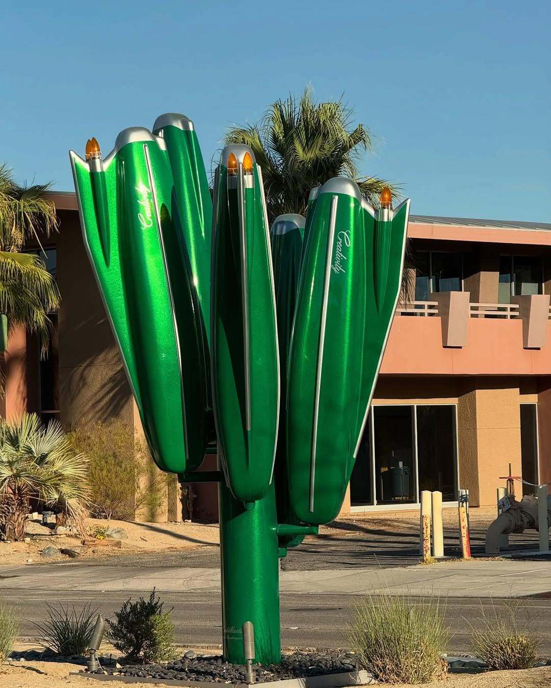 مجسمه بزرگ و سبزرنگ به شکل کاکتوس که از بالههای عقب (Tailfins) خودروهای کلاسیک کادیلاک دهه ۱۹۵۰ و ۱۹۶۰ الهام گرفته شده، و کلمه Creativity (خلاقیت) روی بدنه آن نوشته شده است؛ این اثر هنری در یک محیط بیابانی با درختان نخل و کوههای پسزمینه قرار دارد. مجسمه بزرگ و سبزرنگ به شکل کاکتوس که از بالههای عقب (Tailfins) خودروهای کلاسیک کادیلاک دهه ۱۹۵۰ و ۱۹۶۰ الهام گرفته شده، و کلمه Creativity (خلاقیت) روی بدنه آن نوشته شده است؛ این اثر هنری در یک محیط بیابانی با درختان نخل و کوههای پسزمینه قرار دارد.