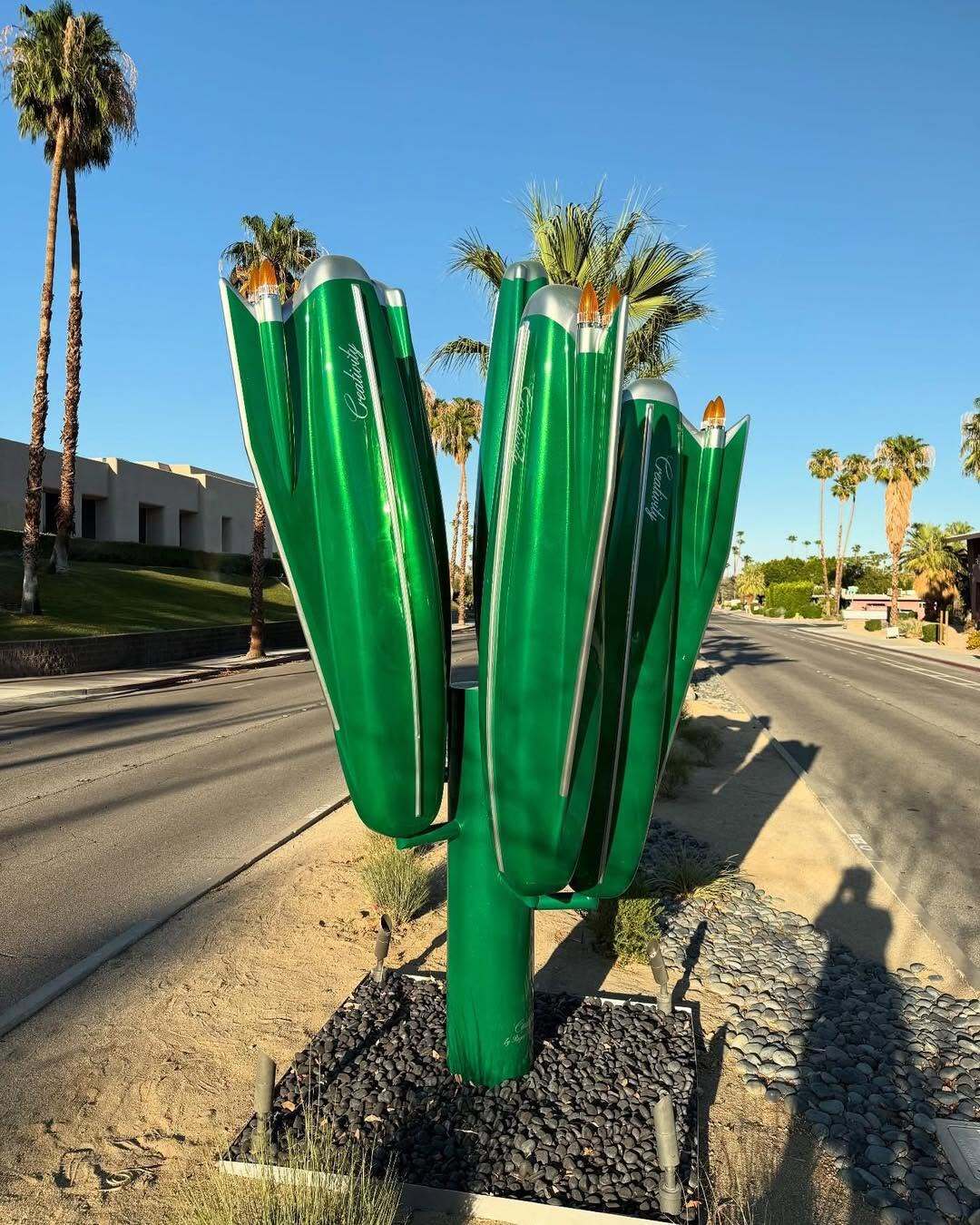 مجسمه بزرگ و سبزرنگ به شکل کاکتوس که از باله‌های عقب (Tailfins) خودروهای کلاسیک کادیلاک دهه ۱۹۵۰ و ۱۹۶۰ الهام گرفته شده، و کلمه Creativity (خلاقیت) روی بدنه آن نوشته شده است؛ این اثر هنری در یک محیط بیابانی با درختان نخل و کوه‌های پس‌زمینه قرار دارد.