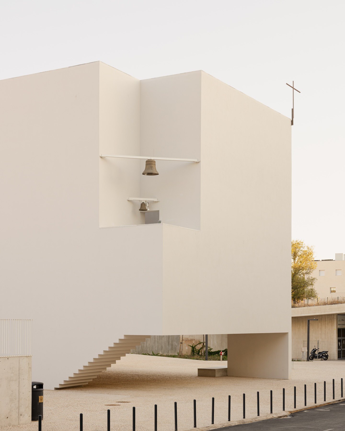 تصویری از نمای داخلی یا بیرونی کلیسای سائو ژوزه دابوآویستا (The Church of São José da Boavista) در پرتغال، با معماری مینیمالیستی نرم و مدرن، که توسط آتلیه بوگیو و ماتوس گامیرو آرکیتکتوس طراحی شده است. تأکید این تصویر بر خطوط تمیز، حجم‌های هندسی ساده و نور