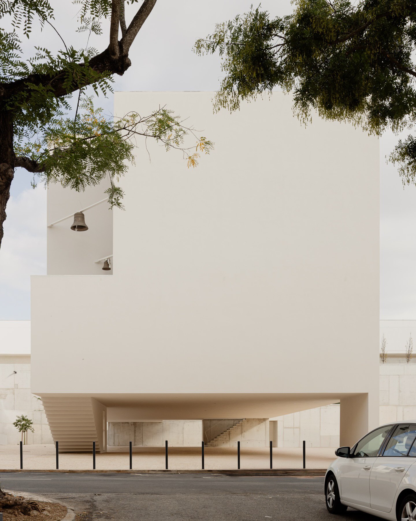 تصویری از نمای داخلی یا بیرونی کلیسای سائو ژوزه دابوآویستا (The Church of São José da Boavista) در پرتغال، با معماری مینیمالیستی نرم و مدرن، که توسط آتلیه بوگیو و ماتوس گامیرو آرکیتکتوس طراحی شده است. تأکید این تصویر بر خطوط تمیز، حجم‌های هندسی ساده و نورپردازی طبیعی است که حس روحانی فضا را نشان می‌دهد.