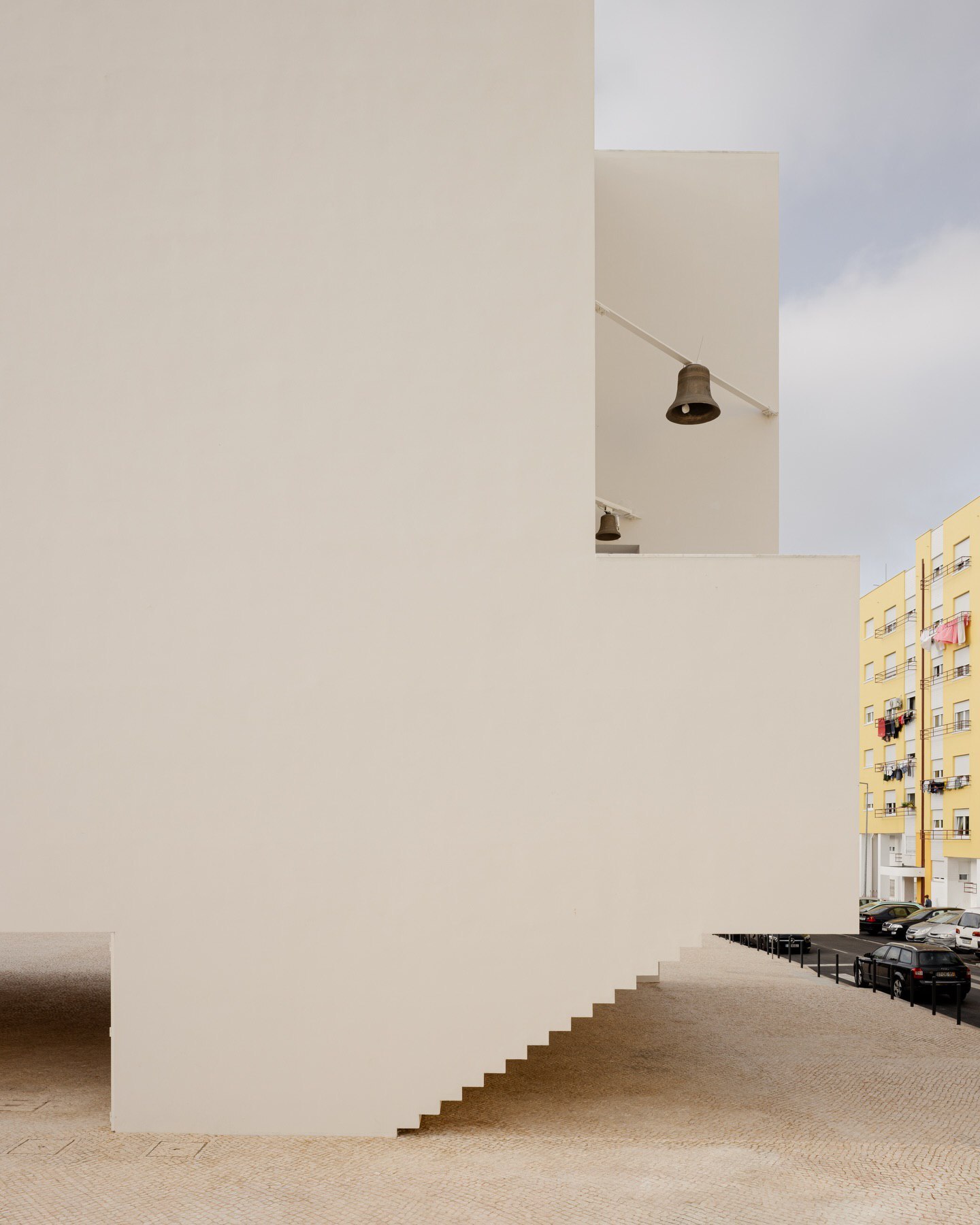 تصویری از نمای داخلی یا بیرونی کلیسای سائو ژوزه دابوآویستا (The Church of São José da Boavista) در پرتغال، با معماری مینیمالیستی نرم و مدرن، که توسط آتلیه بوگیو و ماتوس گامیرو آرکیتکتوس طراحی شده است. تأکید این تصویر بر خطوط تمیز، حجم‌های هندسی ساده و نورپردازی طبیعی است که حس روحانی فضا را نشان می‌دهد.