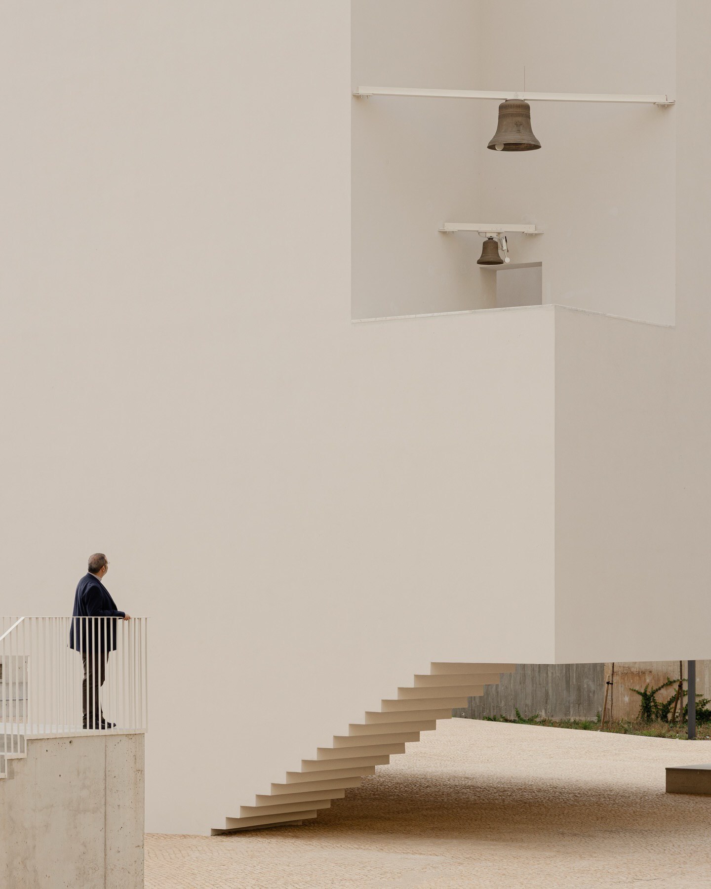 تصویری از نمای داخلی یا بیرونی کلیسای سائو ژوزه دابوآویستا (The Church of São José da Boavista) در پرتغال، با معماری مینیمالیستی نرم و مدرن، که توسط آتلیه بوگیو و ماتوس گامیرو آرکیتکتوس طراحی شده است. تأکید این تصویر بر خطوط تمیز، حجم‌های هندسی ساده و نور