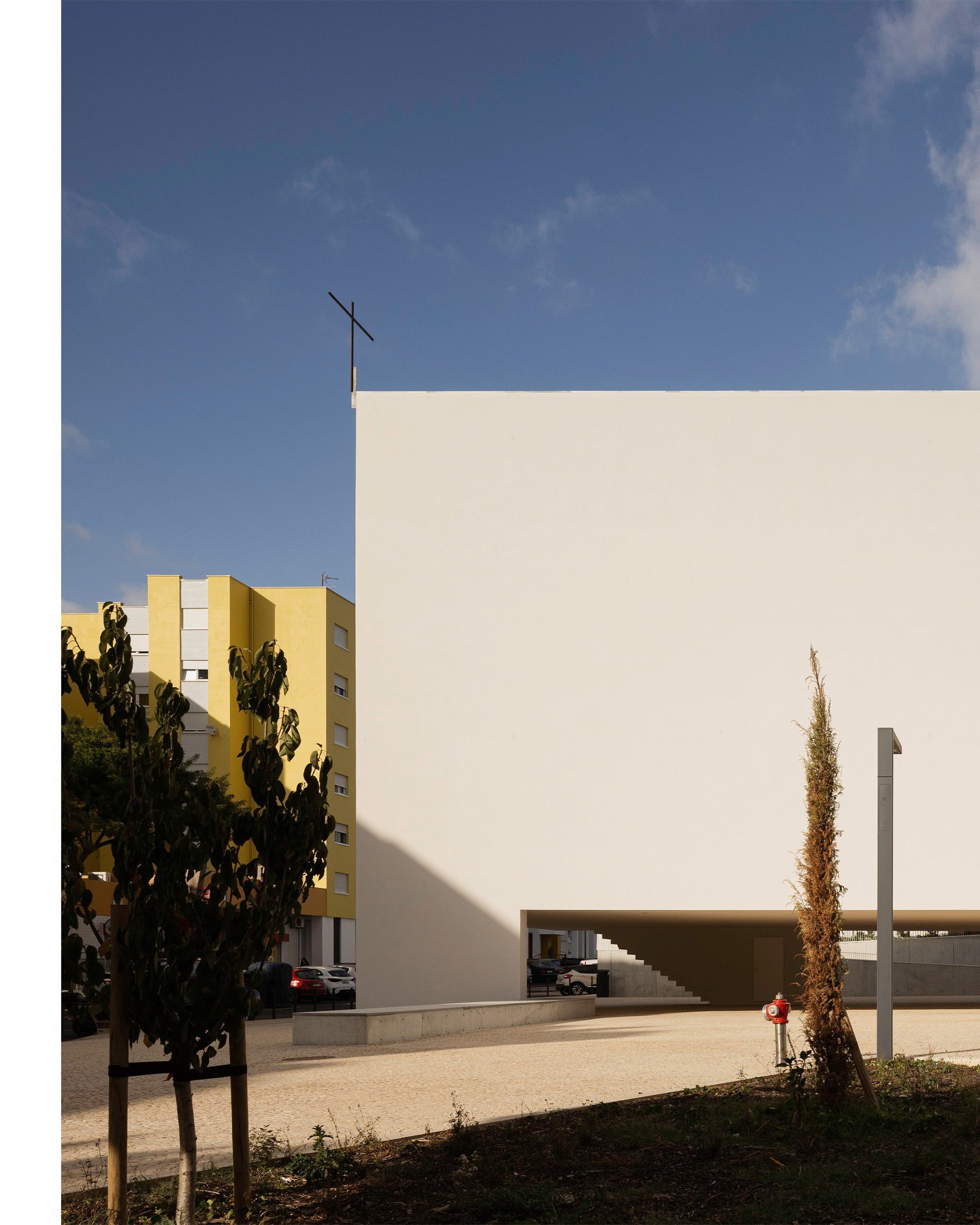 تصویری از نمای داخلی یا بیرونی کلیسای سائو ژوزه دابوآویستا (The Church of São José da Boavista) در پرتغال، با معماری مینیمالیستی نرم و مدرن، که توسط آتلیه بوگیو و ماتوس گامیرو آرکیتکتوس طراحی شده است. تأکید این تصویر بر خطوط تمیز، حجم‌های هندسی ساده و نور