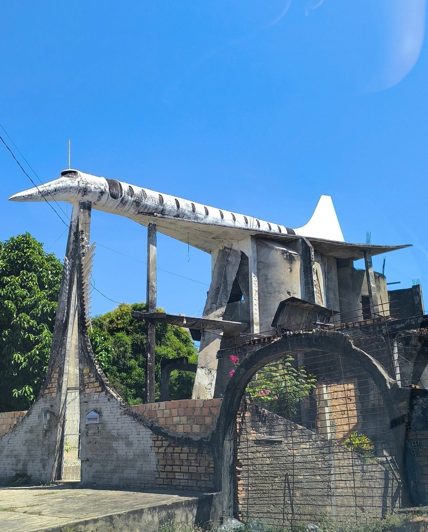 تصویر نمای خارجی ساختمان مسکونی ناتمام در بوآ ویستا، برزیل، که روی سقف آن یک ماکت بتنی بزرگ از هواپیمای کنکورد قرار دارد و با نام «خانه هواپیما» (Casa-Avião) شناخته می‌شود، یادبود رؤیای خلبانی سینوال دی فریتاس اولیویرا.