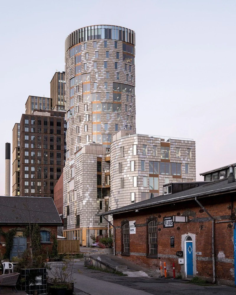 تصویر نمای خارجی و مدرن ساختمان TRÆ (ترا) در بندر آرهوس، دانمارک، که با سیستم سازه‌ای چوبی-هیبریدی و پوشش نمای آلومینیوم بازیافتی توسط Lendager Arkitekter به سبک معماری چرخه‌محور طراحی شده است.