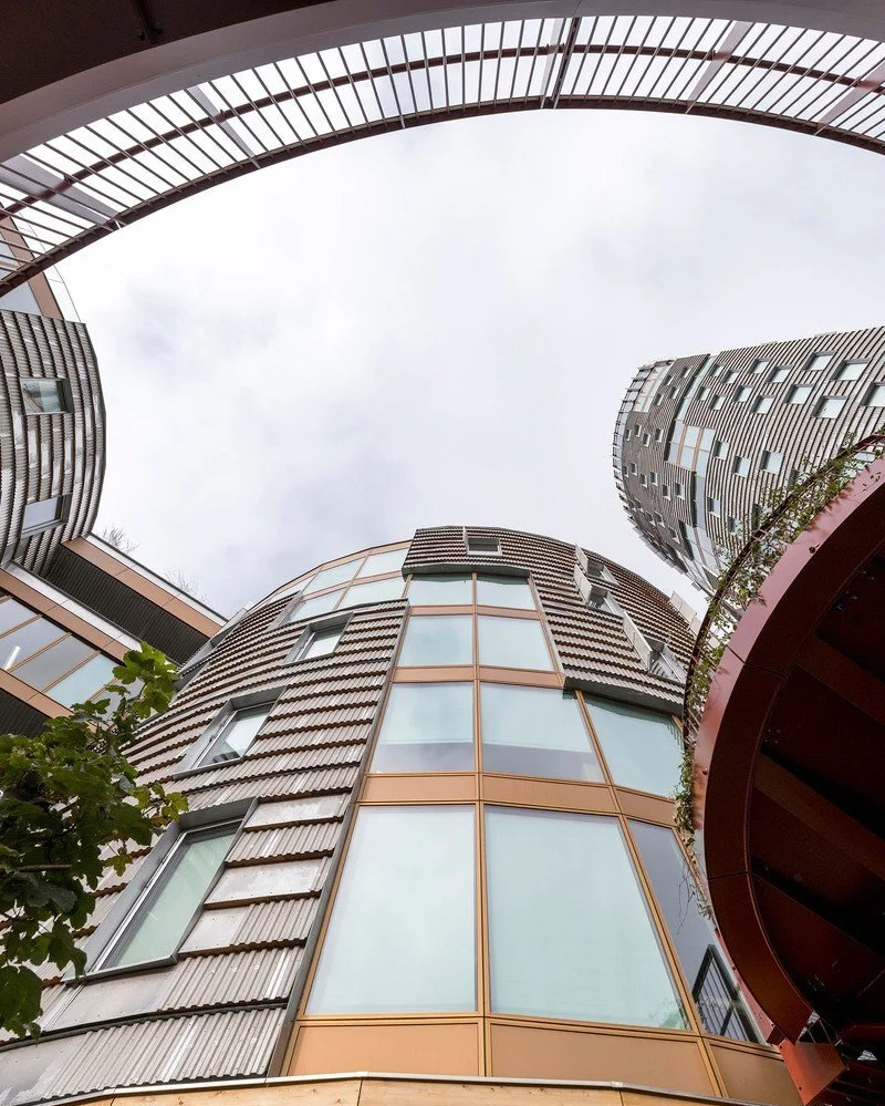 تصویر نمای خارجی و مدرن ساختمان TRÆ (ترا) در بندر آرهوس، دانمارک، که با سیستم سازه‌ای چوبی-هیبریدی و پوشش نمای آلومینیوم بازیافتی توسط Lendager Arkitekter به سبک معماری چرخه‌محور طراحی شده است.