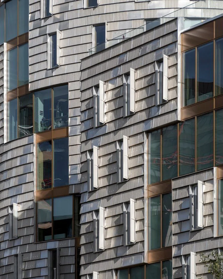 تصویر نمای خارجی و مدرن ساختمان TRÆ (ترا) در بندر آرهوس، دانمارک، که با سیستم سازه‌ای چوبی-هیبریدی و پوشش نمای آلومینیوم بازیافتی توسط Lendager Arkitekter به سبک معماری چرخه‌محور طراحی شده است.