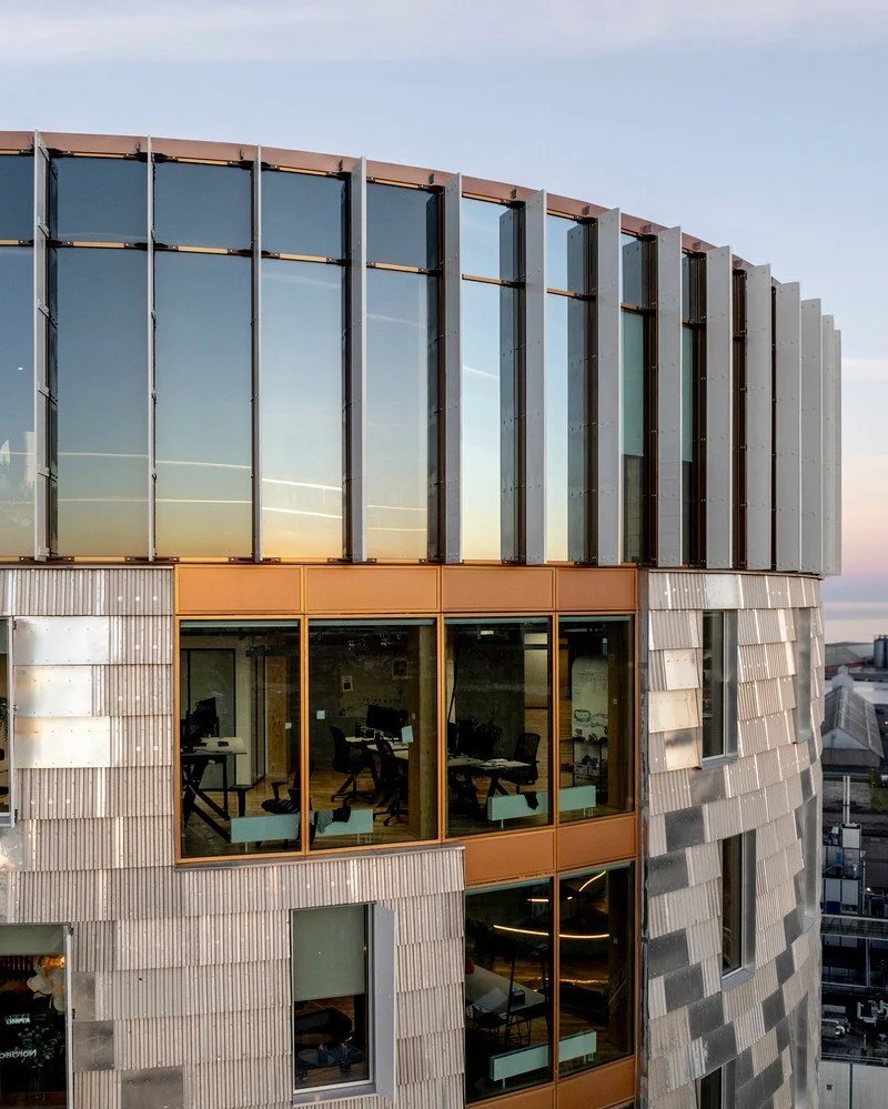 تصویر نمای خارجی و مدرن ساختمان TRÆ (ترا) در بندر آرهوس، دانمارک، که با سیستم سازه‌ای چوبی-هیبریدی و پوشش نمای آلومینیوم بازیافتی توسط Lendager Arkitekter به سبک معماری چرخه‌محور طراحی شده است.