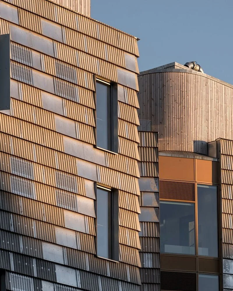 تصویر نمای خارجی و مدرن ساختمان TRÆ (ترا) در بندر آرهوس، دانمارک، که با سیستم سازه‌ای چوبی-هیبریدی و پوشش نمای آلومینیوم بازیافتی توسط Lendager Arkitekter به سبک معماری چرخه‌محور طراحی شده است.