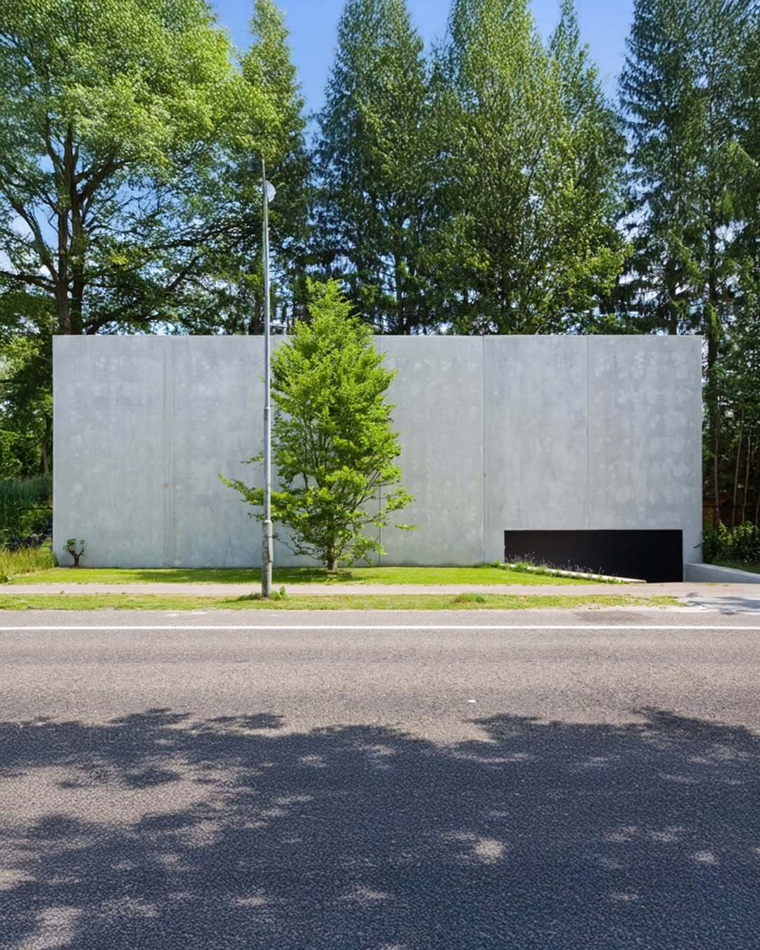 تصویر معماری مدرن و خطی یک خانه در بلژیک که نمای جلویی آن توسط بتن مستحکم پوشیده شده است، اما نمای پشتی کاملاً شیشه‌ای بوده و چشم‌اندازی بی‌نظیر به کانال آبی «کِمپیشه» را به نمایش می‌گذارد.