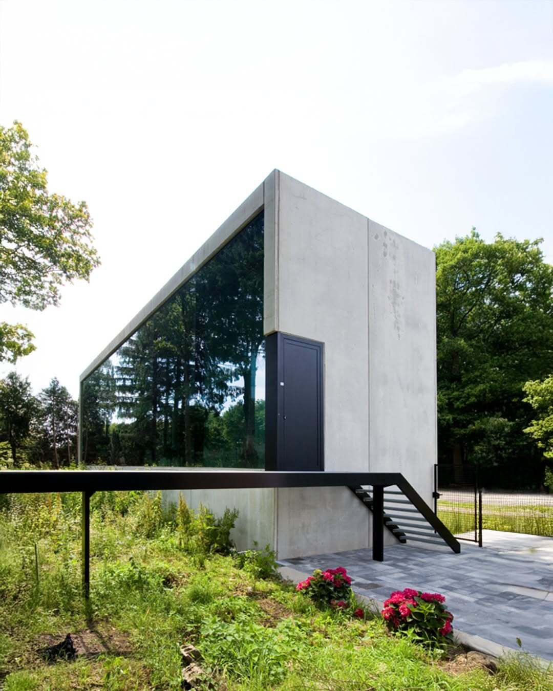 تصویر معماری مدرن و خطی یک خانه در بلژیک که نمای جلویی آن توسط بتن مستحکم پوشیده شده است، اما نمای پشتی کاملاً شیشه‌ای بوده و چشم‌اندازی بی‌نظیر به کانال آبی «کِمپیشه» را به نمایش می‌گذارد.