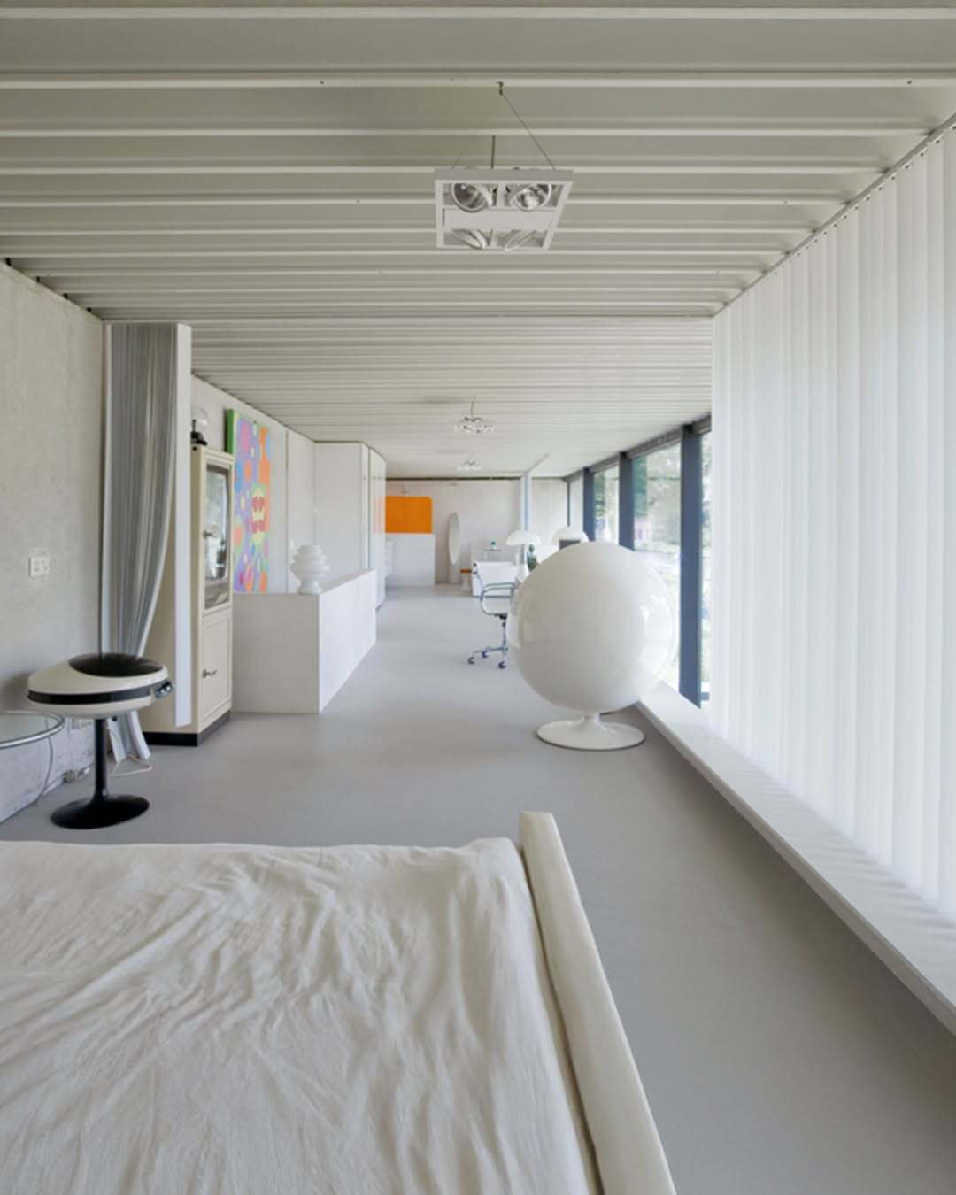 تصویر معماری مدرن و خطی یک خانه در بلژیک که نمای جلویی آن توسط بتن مستحکم پوشیده شده است، اما نمای پشتی کاملاً شیشه‌ای بوده و چشم‌اندازی بی‌نظیر به کانال آبی «کِمپیشه» را به نمایش می‌گذارد.