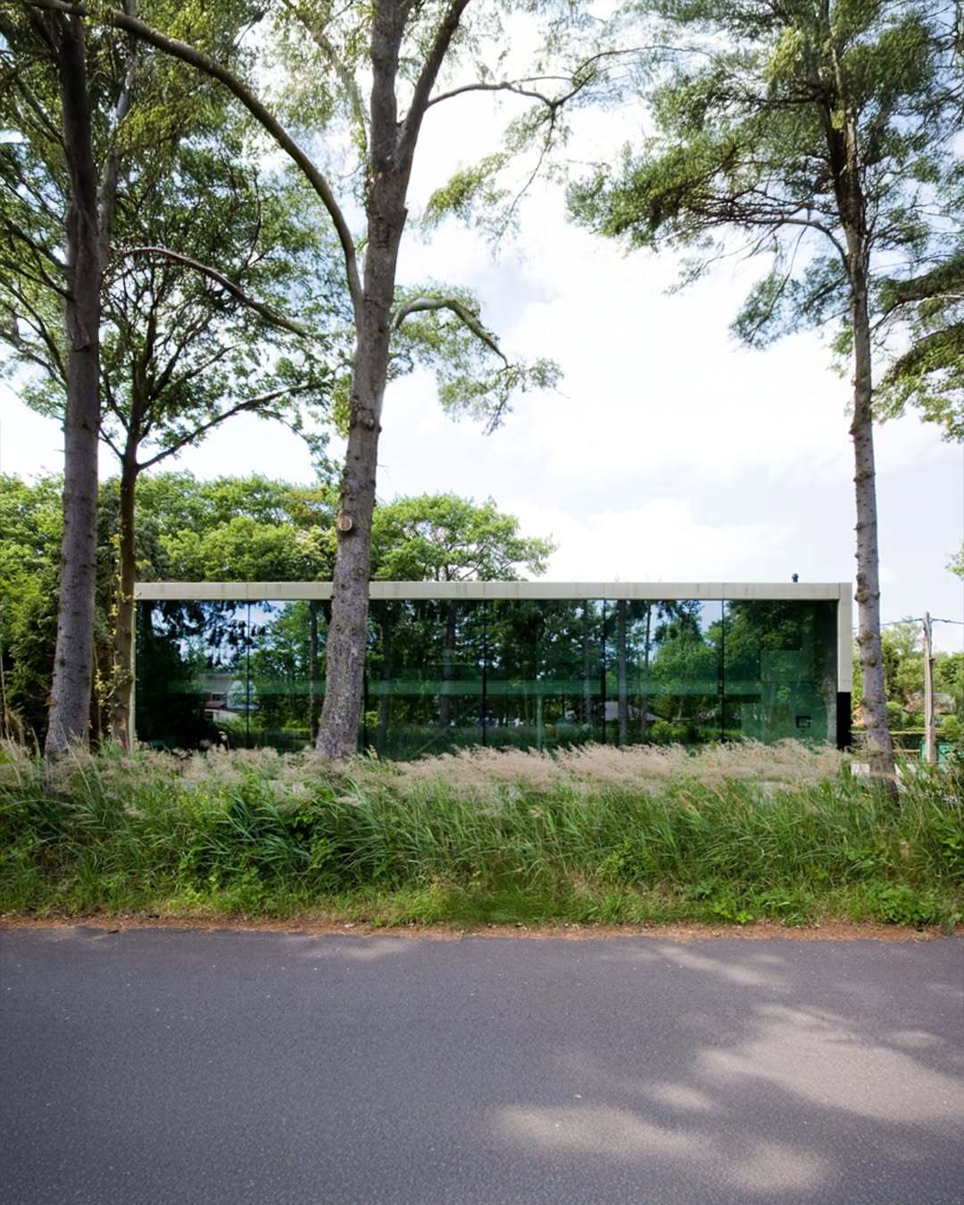 تصویر معماری مدرن و خطی یک خانه در بلژیک که نمای جلویی آن توسط بتن مستحکم پوشیده شده است، اما نمای پشتی کاملاً شیشه‌ای بوده و چشم‌اندازی بی‌نظیر به کانال آبی «کِمپیشه» را به نمایش می‌گذارد.