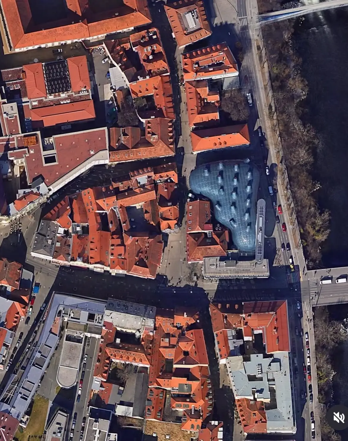 تصویری از نمای خارجی ساختمان موزه هنر کونست‌هاوس (Kunsthaus) در گراتس اتریش، که ساختار ارگانیک و غیرمعمول آن شبیه به یک موجود زنده با پوسته آبی رنگ است و به عنوان یک نماد معماری مدرن و «بیگانه دوست» طراحی شده توسط کولین فورنیر و پیتر کوک شناخته می‌شود.