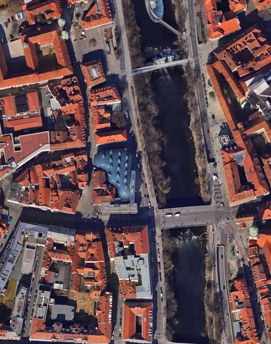 تصویری از نمای خارجی ساختمان موزه هنر کونست‌هاوس (Kunsthaus) در گراتس اتریش، که ساختار ارگانیک و غیرمعمول آن شبیه به یک موجود زنده با پوسته آبی رنگ است و به عنوان یک نماد معماری مدرن و «بیگانه دوست» طراحی شده توسط کولین فورنیر و پیتر کوک شناخته می‌شود.