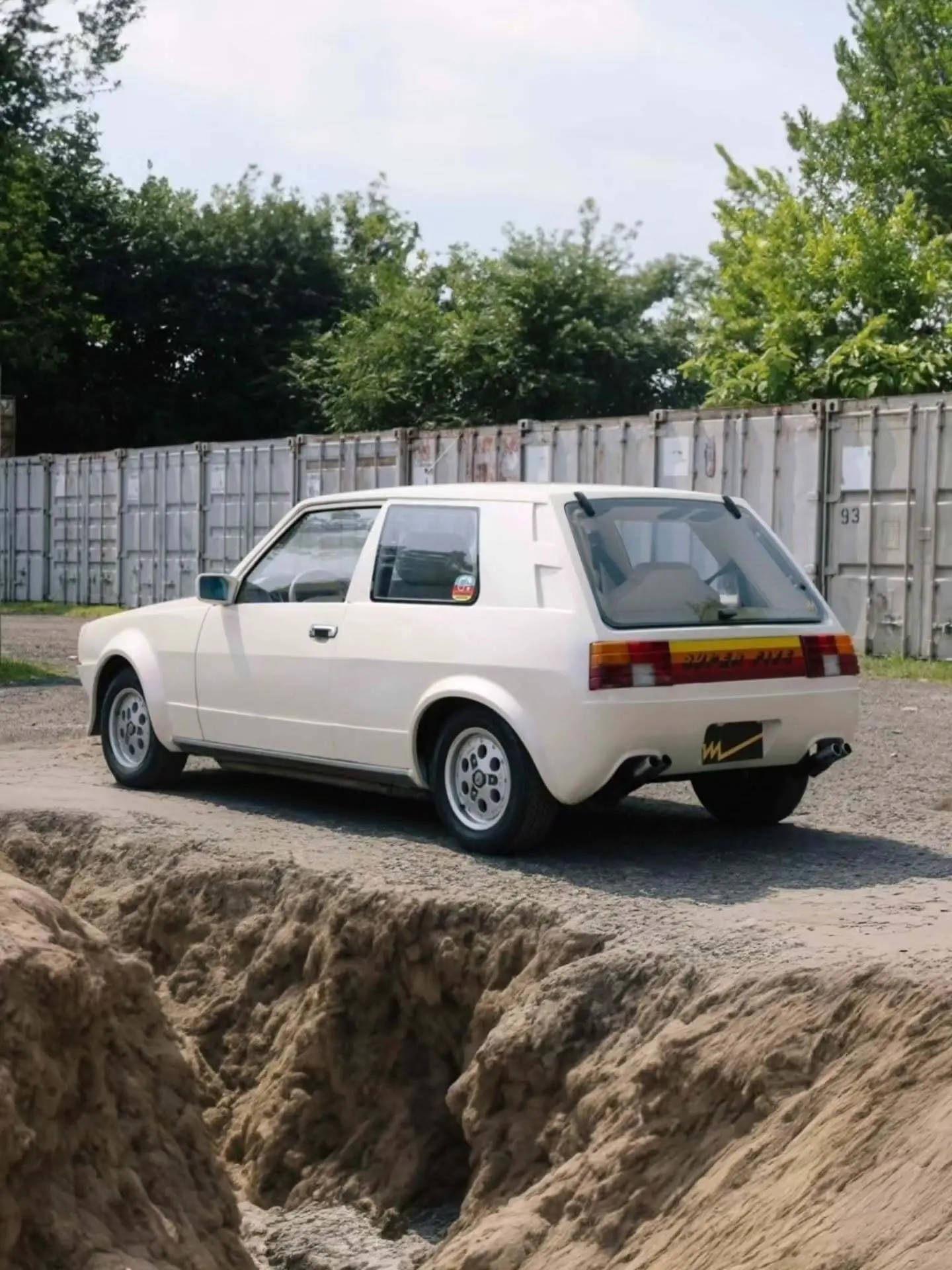 تصویر خودروی کلاسیک و نایاب اسبارو سوپر فایو (Sbarro Super Five) مدل ۱۹۸۵ با بدنه پهن سفید و چراغهای جلو چهارگانه در یک منظره کوهستانی. تصویر خودروی کلاسیک و نایاب اسبارو سوپر فایو (Sbarro Super Five) مدل ۱۹۸۵ با بدنه پهن سفید و چراغهای جلو چهارگانه در یک منظره کوهستانی.