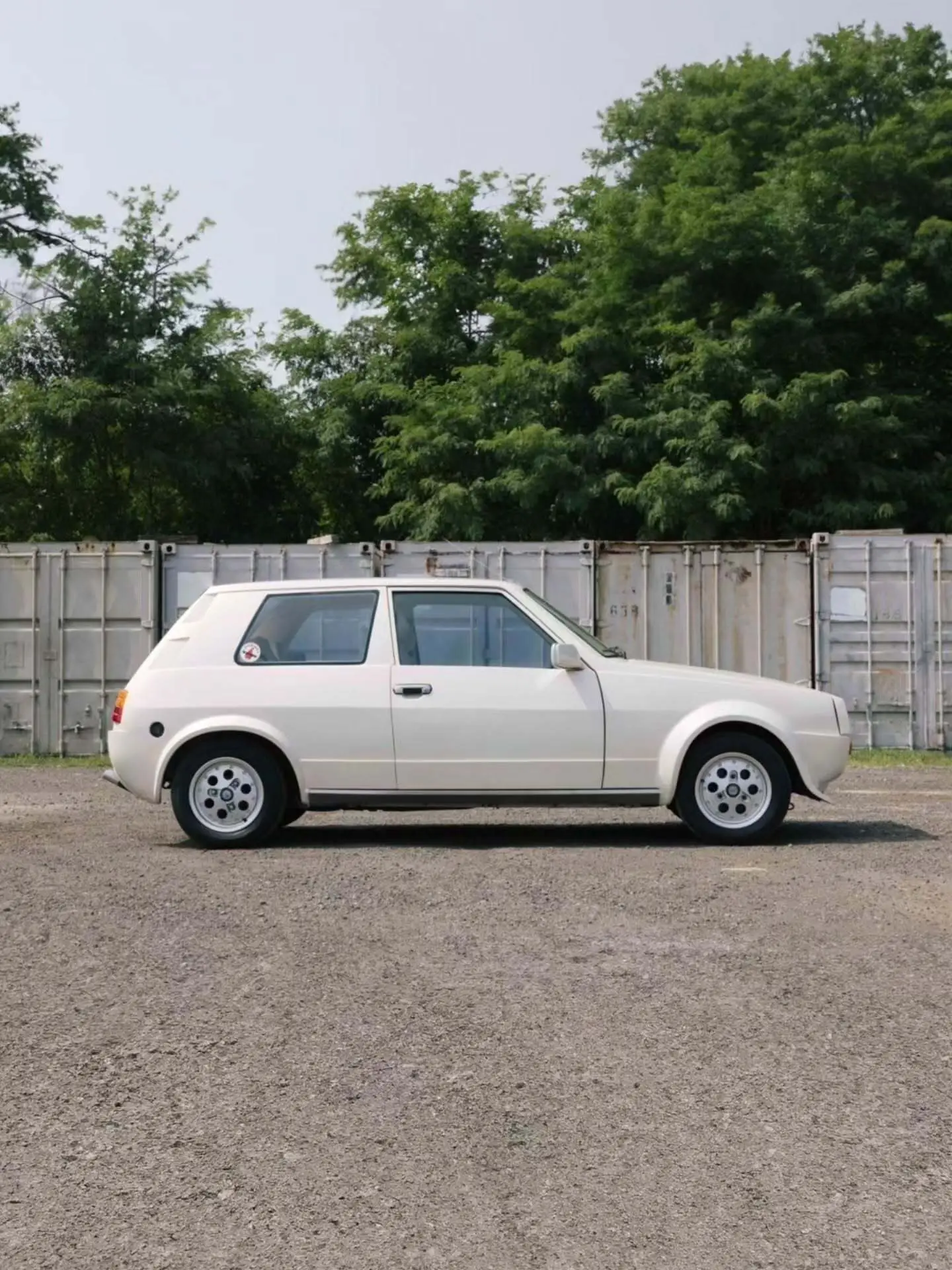 تصویر خودروی کلاسیک و نایاب اسبارو سوپر فایو (Sbarro Super Five) مدل ۱۹۸۵ با بدنه پهن سفید و چراغ‌های جلو چهارگانه در یک منظره کوهستانی.