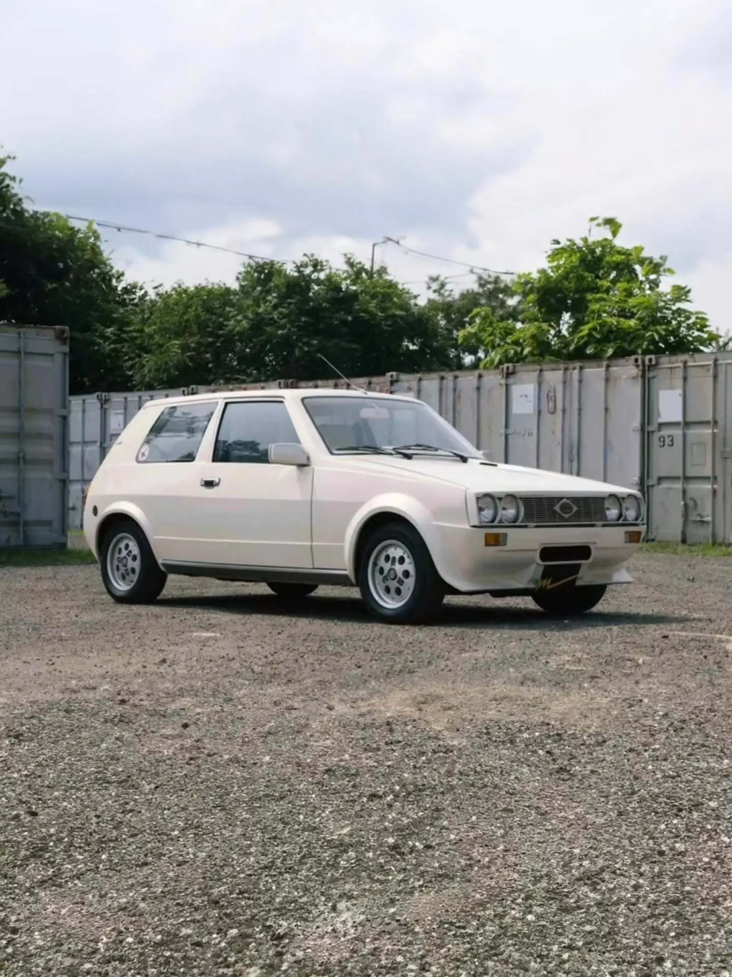 تصویر خودروی کلاسیک و نایاب اسبارو سوپر فایو (Sbarro Super Five) مدل ۱۹۸۵ با بدنه پهن سفید و چراغ‌های جلو چهارگانه در یک منظره کوهستانی.