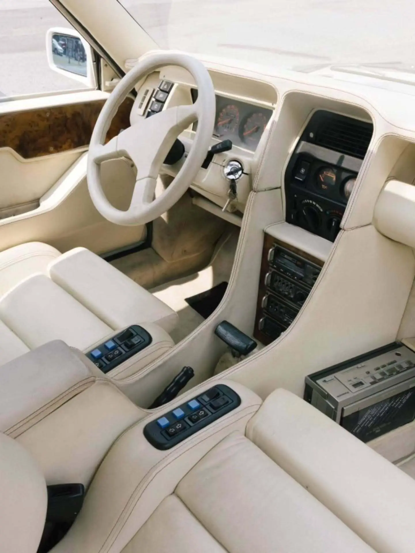 تصویر خودروی کلاسیک و نایاب اسبارو سوپر فایو (Sbarro Super Five) مدل ۱۹۸۵ با بدنه پهن سفید و چراغ‌های جلو چهارگانه در یک منظره کوهستانی.