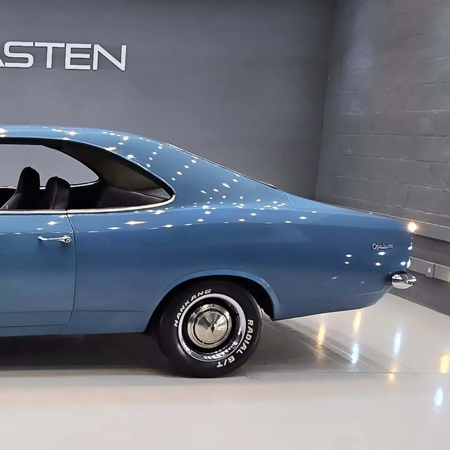 نمای کناری و موتور ارتقایافته شورولت اوپالا ۲۵۰۰ مدل ۱۹۷۶ توربو به رنگ سفید با رینگ‌های کلاسیک و کیت بدنه فابریک در وضعیت نمایشگاهی.