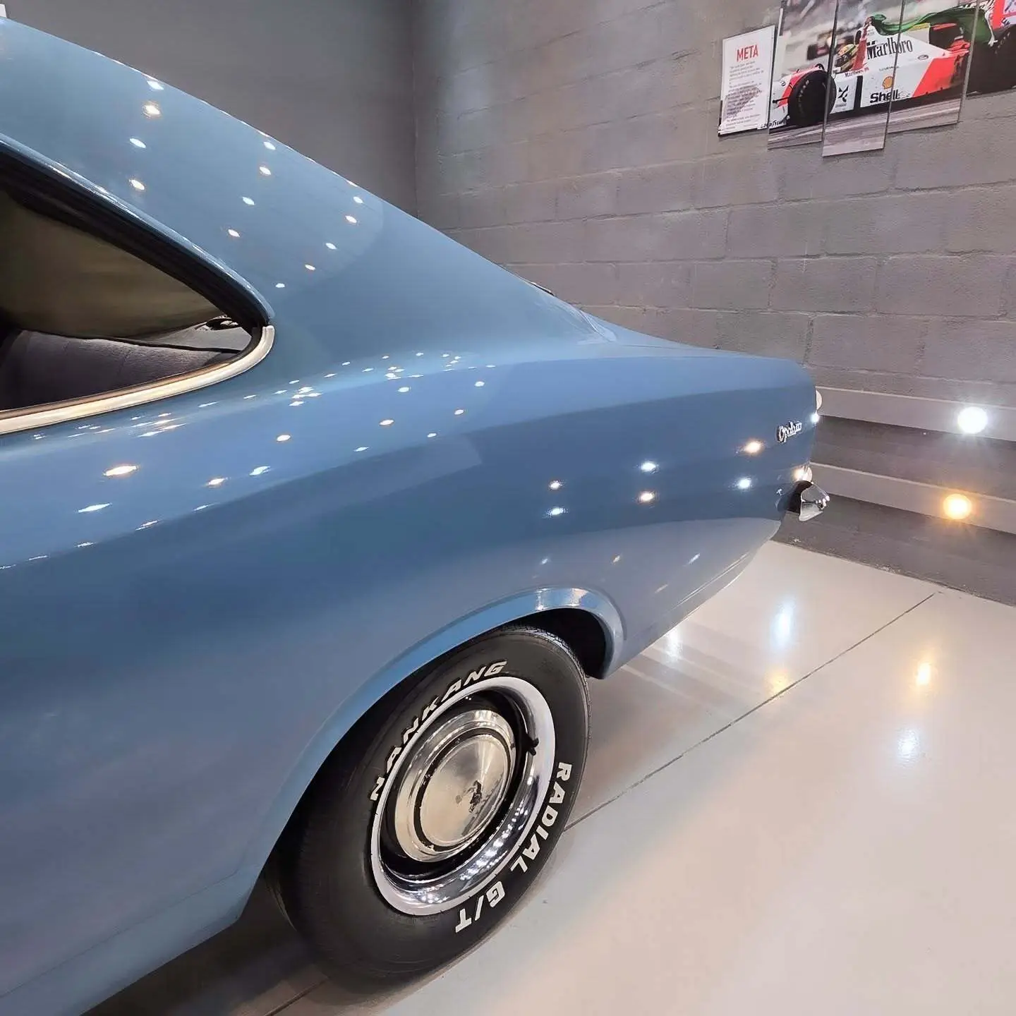 نمای کناری و موتور ارتقایافته شورولت اوپالا ۲۵۰۰ مدل ۱۹۷۶ توربو به رنگ سفید با رینگ‌های کلاسیک و کیت بدنه فابریک در وضعیت نمایشگاهی.