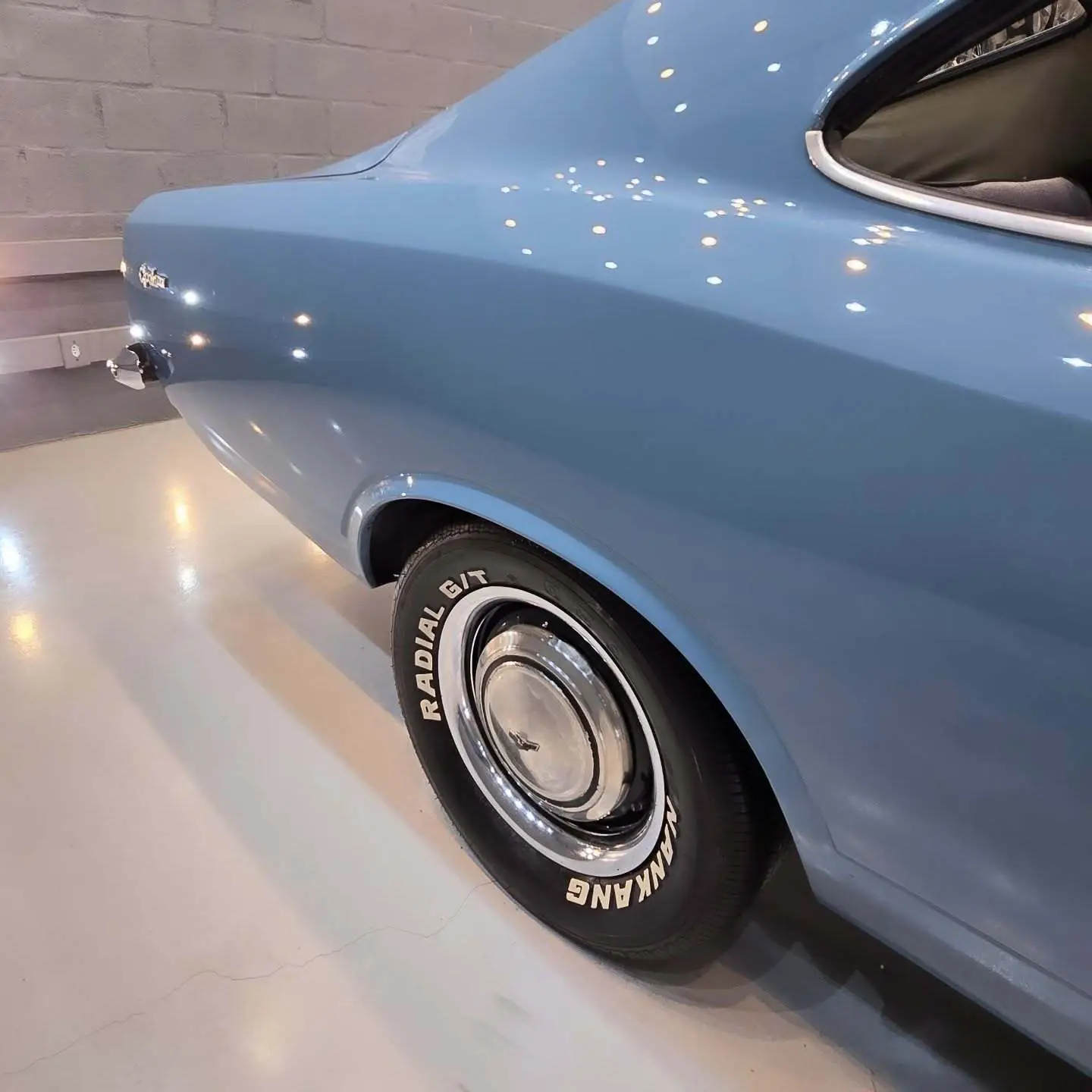 نمای کناری و موتور ارتقایافته شورولت اوپالا ۲۵۰۰ مدل ۱۹۷۶ توربو به رنگ سفید با رینگ‌های کلاسیک و کیت بدنه فابریک در وضعیت نمایشگاهی.