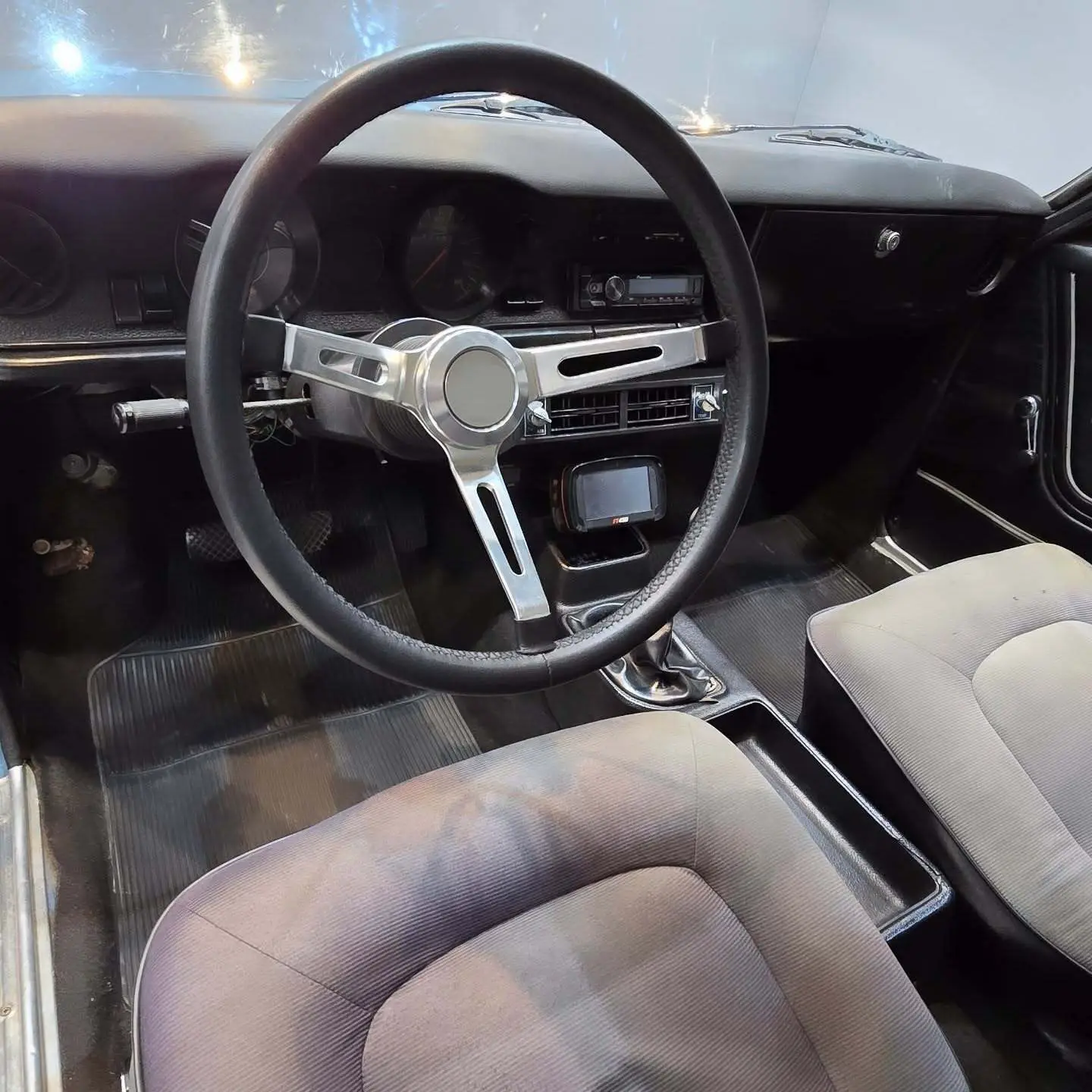 نمای کناری و موتور ارتقایافته شورولت اوپالا ۲۵۰۰ مدل ۱۹۷۶ توربو به رنگ سفید با رینگ‌های کلاسیک و کیت بدنه فابریک در وضعیت نمایشگاهی.