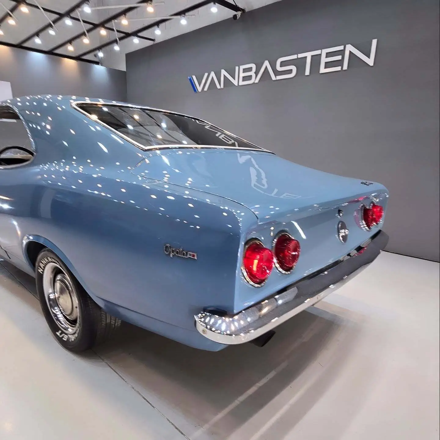 نمای کناری و موتور ارتقایافته شورولت اوپالا ۲۵۰۰ مدل ۱۹۷۶ توربو به رنگ سفید با رینگ‌های کلاسیک و کیت بدنه فابریک در وضعیت نمایشگاهی.