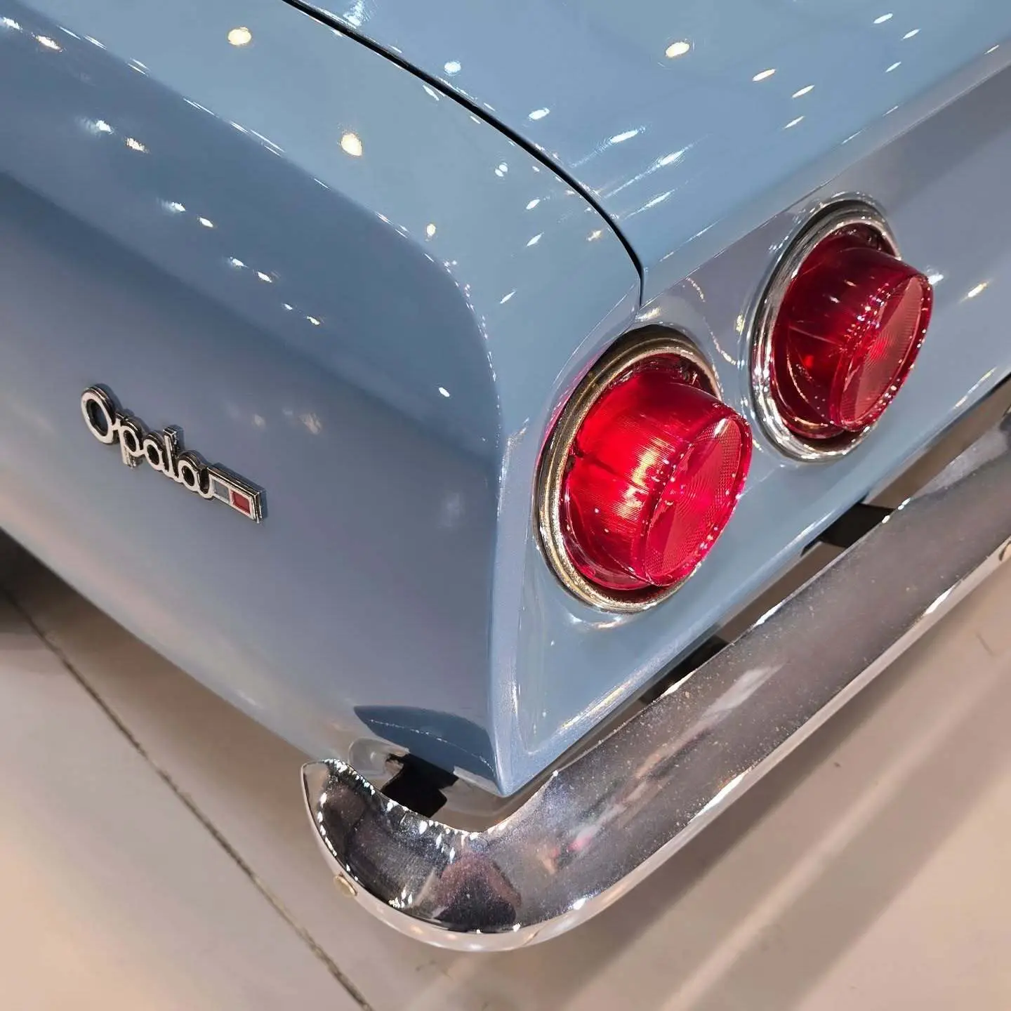 نمای کناری و موتور ارتقایافته شورولت اوپالا ۲۵۰۰ مدل ۱۹۷۶ توربو به رنگ سفید با رینگ‌های کلاسیک و کیت بدنه فابریک در وضعیت نمایشگاهی.