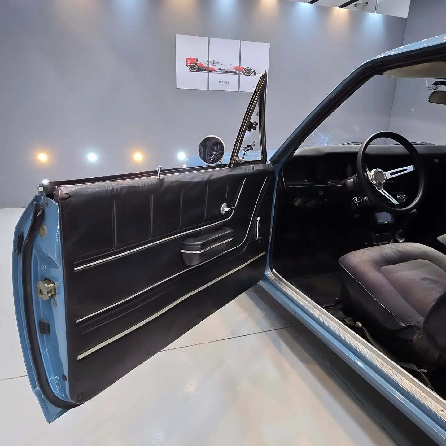 نمای کناری و موتور ارتقایافته شورولت اوپالا ۲۵۰۰ مدل ۱۹۷۶ توربو به رنگ سفید با رینگ‌های کلاسیک و کیت بدنه فابریک در وضعیت نمایشگاهی.