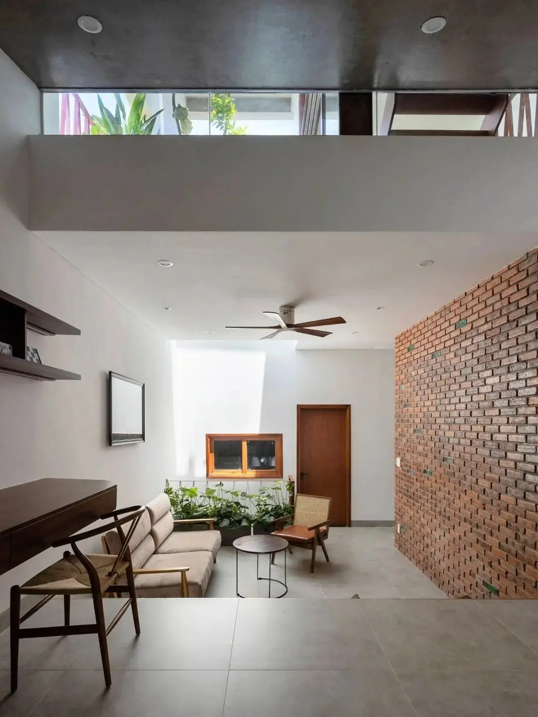 نمای خارجی مدرن خانه برنج قهوه‌ای با ترکیب آجرهای سفالی ترکوتا، بلوک‌های شیشه‌ای رنگی و فضای سبز که نشان‌دهنده معماری پایدار و نورپردازی طبیعی است.