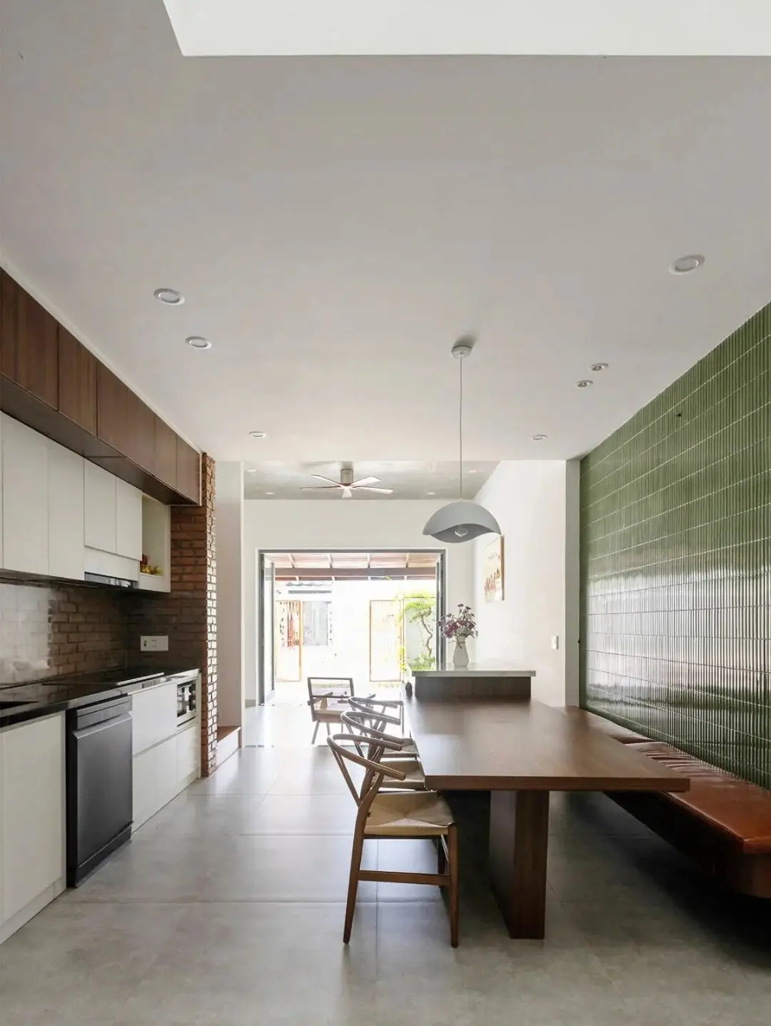 نمای خارجی مدرن خانه برنج قهوه‌ای با ترکیب آجرهای سفالی ترکوتا، بلوک‌های شیشه‌ای رنگی و فضای سبز که نشان‌دهنده معماری پایدار و نورپردازی طبیعی است.