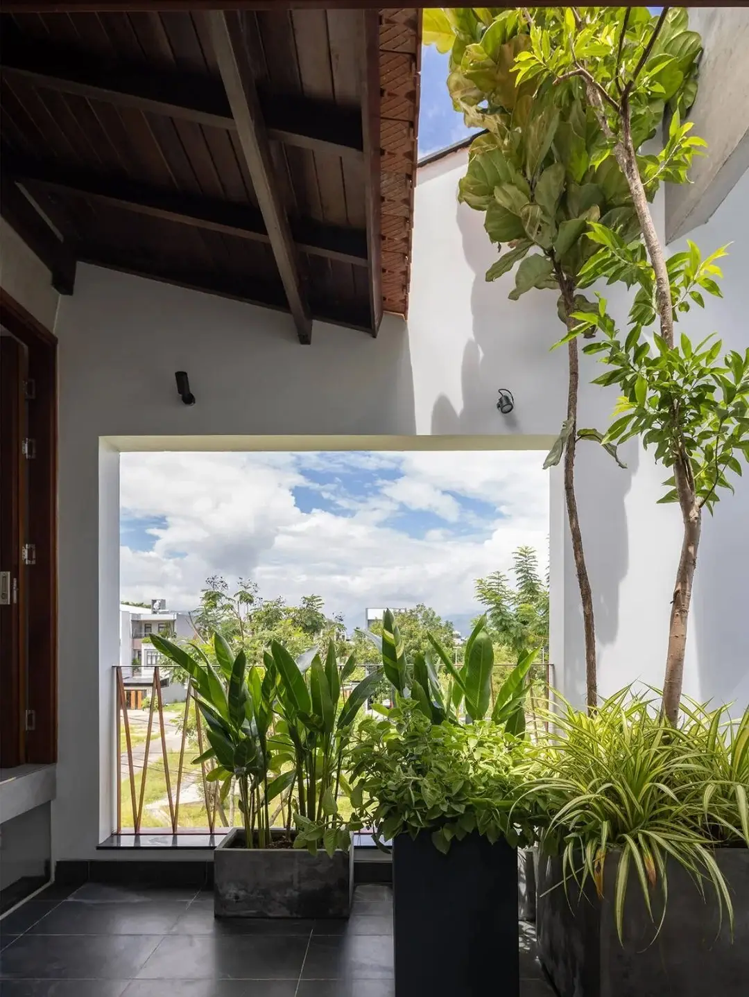 نمای خارجی مدرن خانه برنج قهوه‌ای با ترکیب آجرهای سفالی ترکوتا، بلوک‌های شیشه‌ای رنگی و فضای سبز که نشان‌دهنده معماری پایدار و نورپردازی طبیعی است.