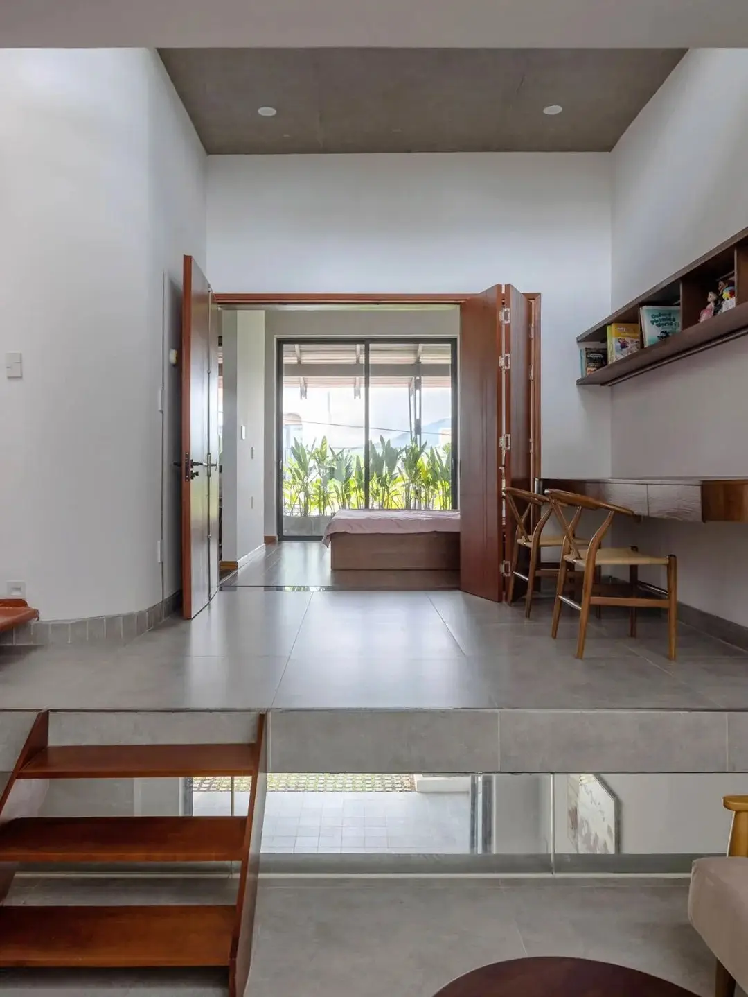 نمای خارجی مدرن خانه برنج قهوه‌ای با ترکیب آجرهای سفالی ترکوتا، بلوک‌های شیشه‌ای رنگی و فضای سبز که نشان‌دهنده معماری پایدار و نورپردازی طبیعی است.