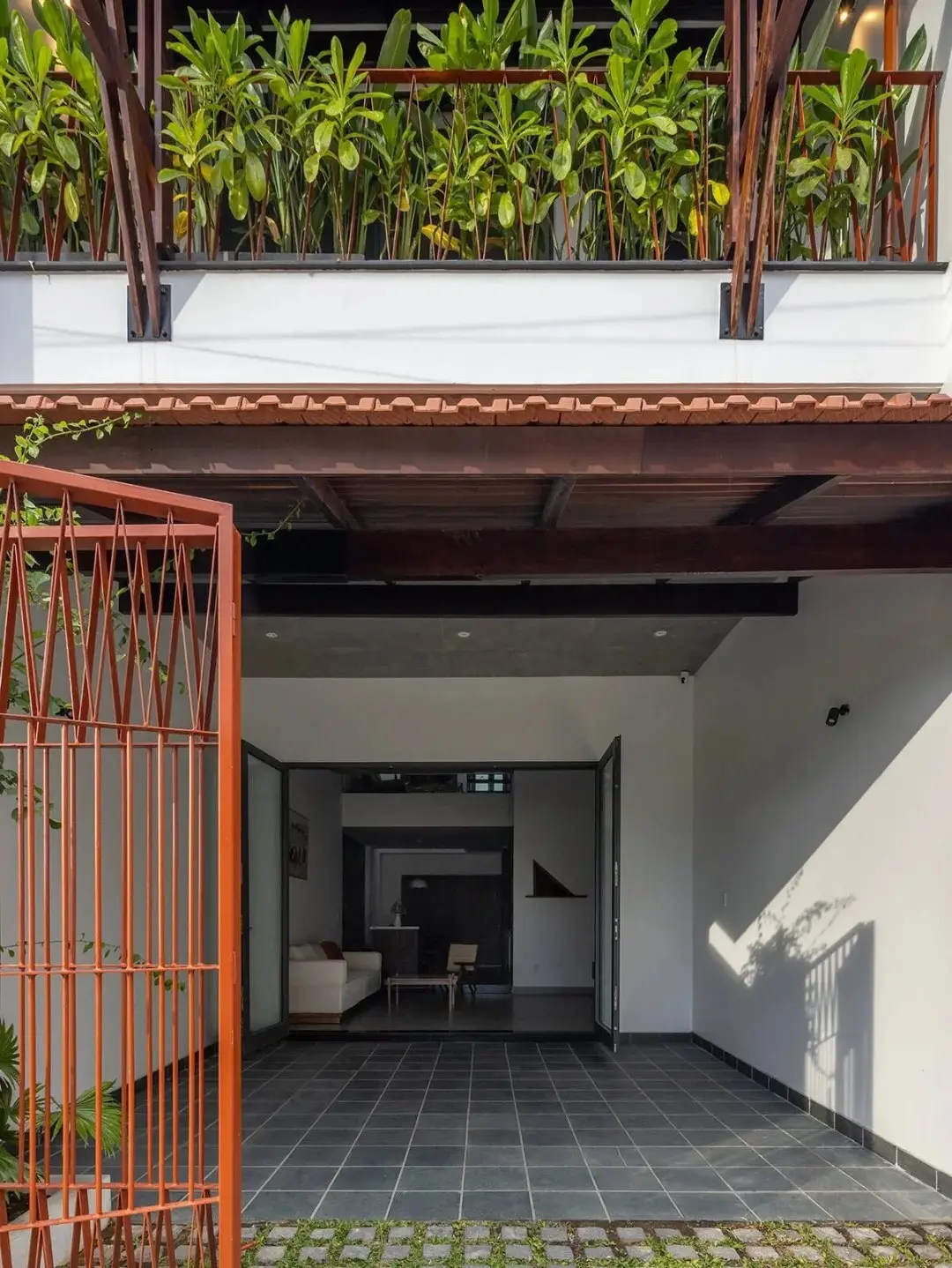 نمای خارجی مدرن خانه برنج قهوه‌ای با ترکیب آجرهای سفالی ترکوتا، بلوک‌های شیشه‌ای رنگی و فضای سبز که نشان‌دهنده معماری پایدار و نورپردازی طبیعی است.