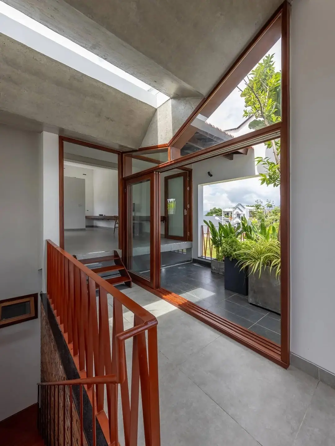 نمای خارجی مدرن خانه برنج قهوه‌ای با ترکیب آجرهای سفالی ترکوتا، بلوک‌های شیشه‌ای رنگی و فضای سبز که نشان‌دهنده معماری پایدار و نورپردازی طبیعی است.