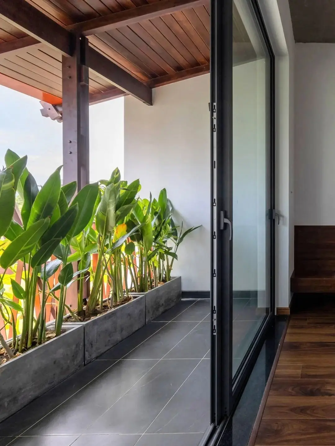 نمای خارجی مدرن خانه برنج قهوه‌ای با ترکیب آجرهای سفالی ترکوتا، بلوک‌های شیشه‌ای رنگی و فضای سبز که نشان‌دهنده معماری پایدار و نورپردازی طبیعی است.