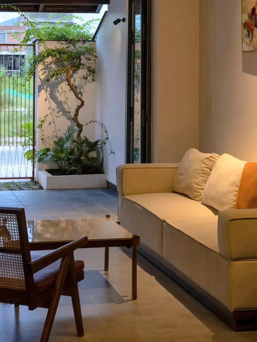 نمای خارجی مدرن خانه برنج قهوه‌ای با ترکیب آجرهای سفالی ترکوتا، بلوک‌های شیشه‌ای رنگی و فضای سبز که نشان‌دهنده معماری پایدار و نورپردازی طبیعی است.