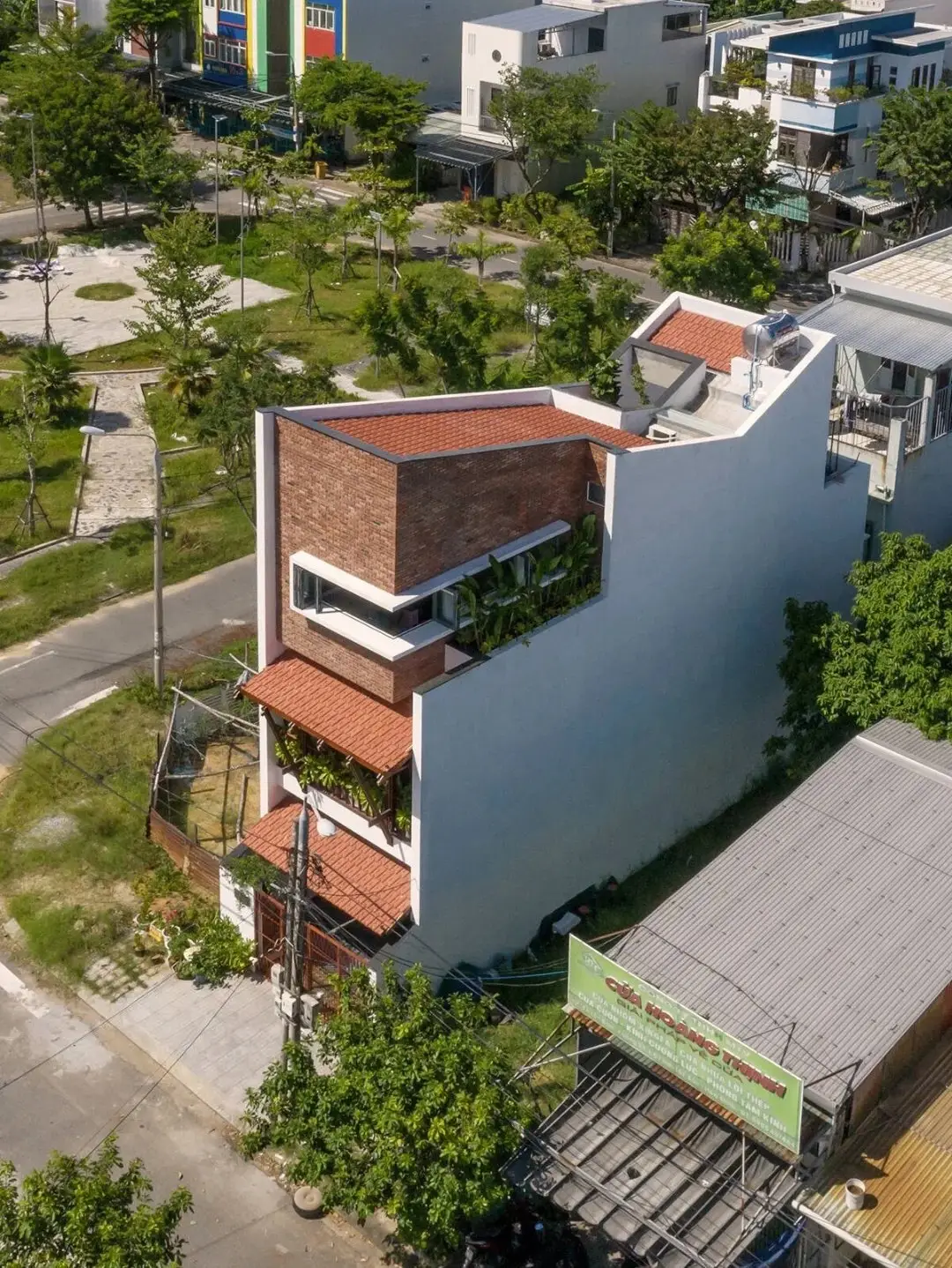 نمای خارجی مدرن خانه برنج قهوه‌ای با ترکیب آجرهای سفالی ترکوتا، بلوک‌های شیشه‌ای رنگی و فضای سبز که نشان‌دهنده معماری پایدار و نورپردازی طبیعی است.