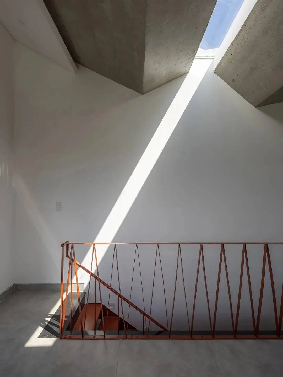 نمای خارجی مدرن خانه برنج قهوه‌ای با ترکیب آجرهای سفالی ترکوتا، بلوک‌های شیشه‌ای رنگی و فضای سبز که نشان‌دهنده معماری پایدار و نورپردازی طبیعی است.