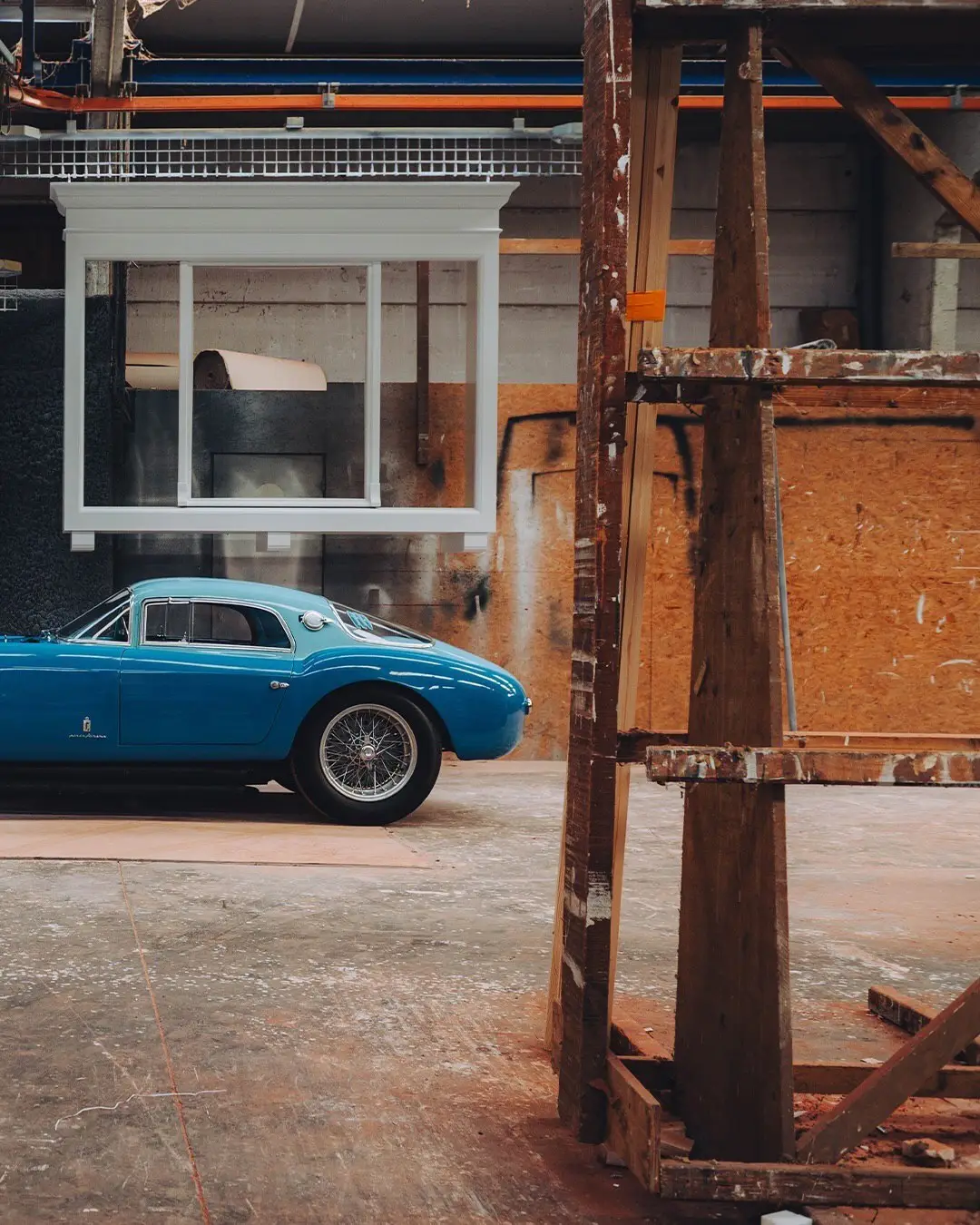 نمای جلویی و جانبی خودروی کلاسیک مازراتی A6GCS فارینا برلینتا به رنگ آبی متالیک با رینگ‌های پره‌ای در مقابل یک بنای سنتی اروپایی.