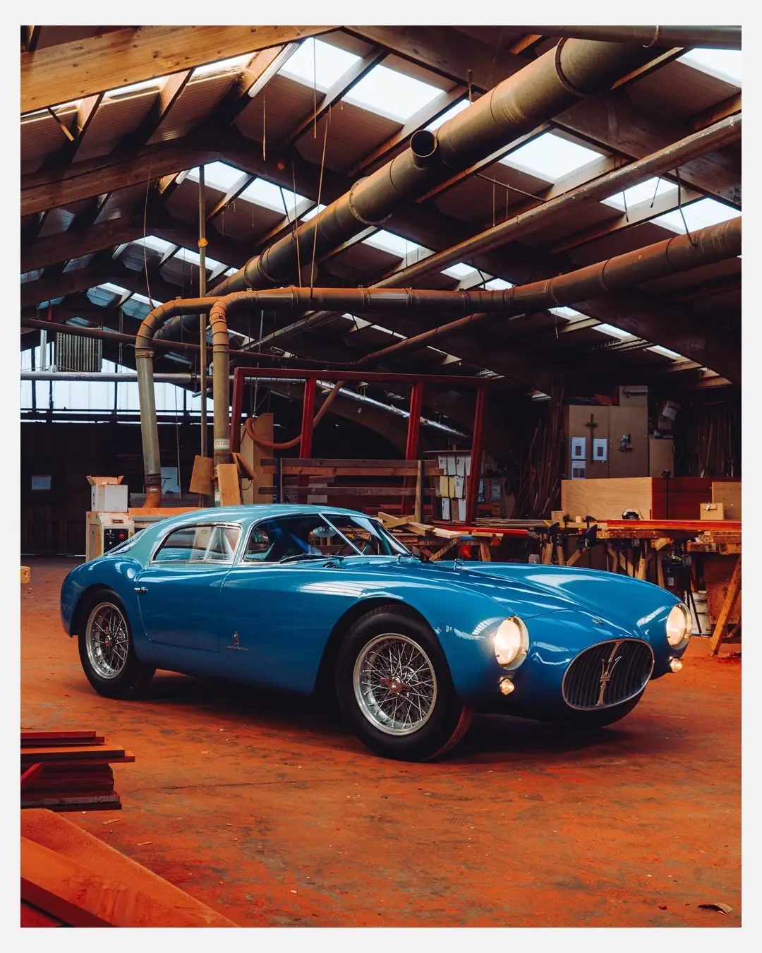 نمای جلویی و جانبی خودروی کلاسیک مازراتی A6GCS فارینا برلینتا به رنگ آبی متالیک با رینگ‌های پره‌ای در مقابل یک بنای سنتی اروپایی.