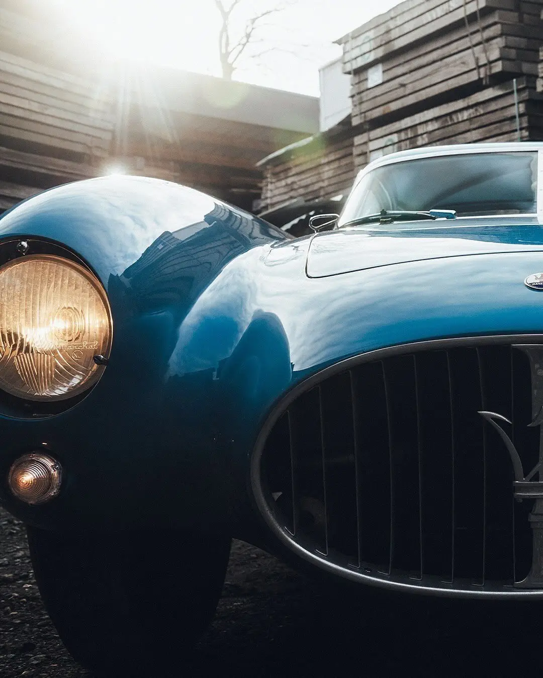 نمای جلویی و جانبی خودروی کلاسیک مازراتی A6GCS فارینا برلینتا به رنگ آبی متالیک با رینگ‌های پره‌ای در مقابل یک بنای سنتی اروپایی.